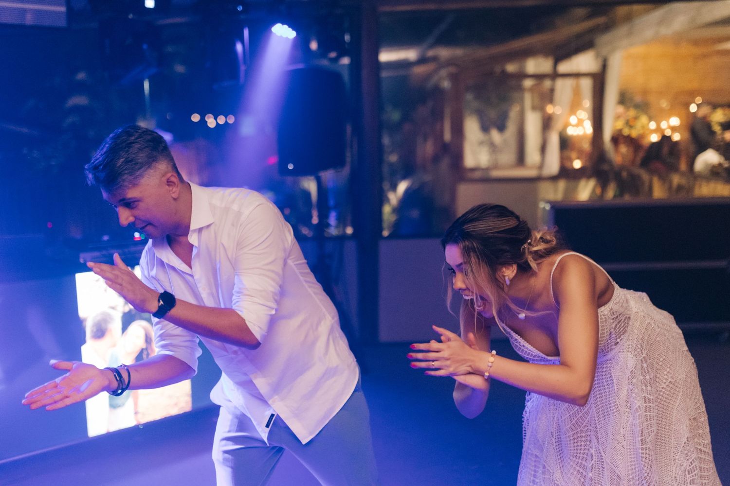 Dancing couple enjoying a lively moment at a wedding reception with blue lighting.