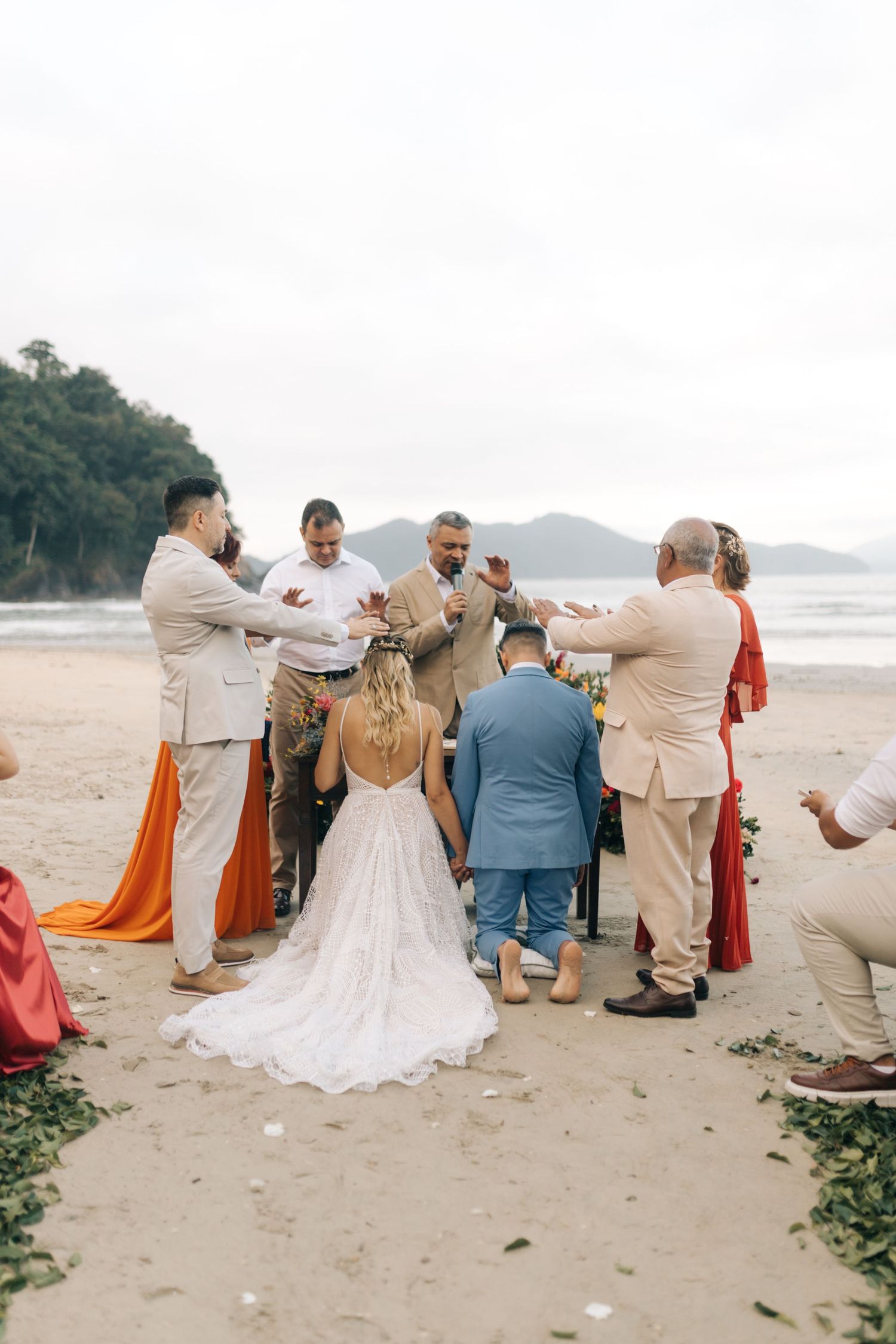Wedding party celebrates on a sandy beach with mountains visible in the background.