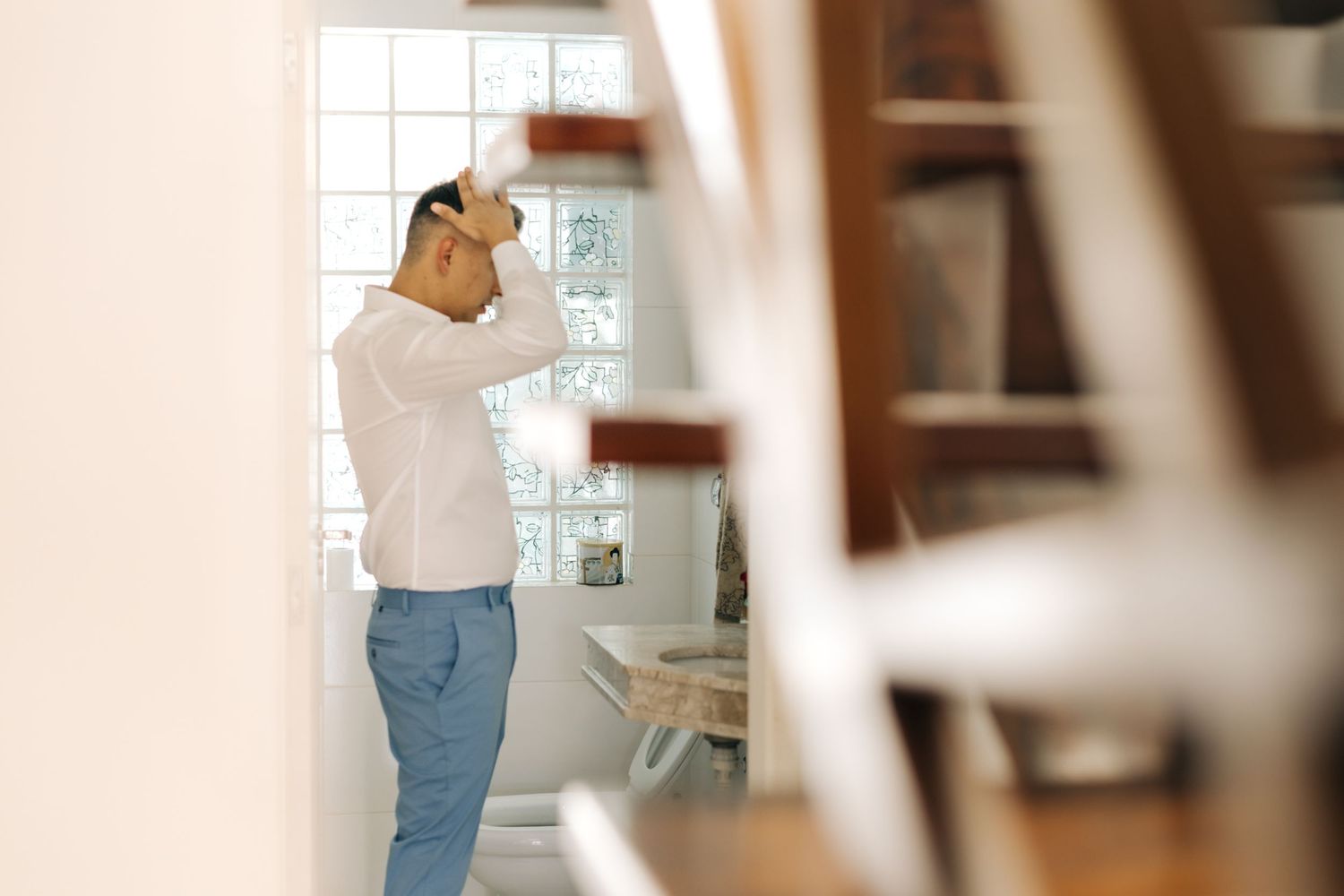 Person in casual attire standing by window in bright interior space.