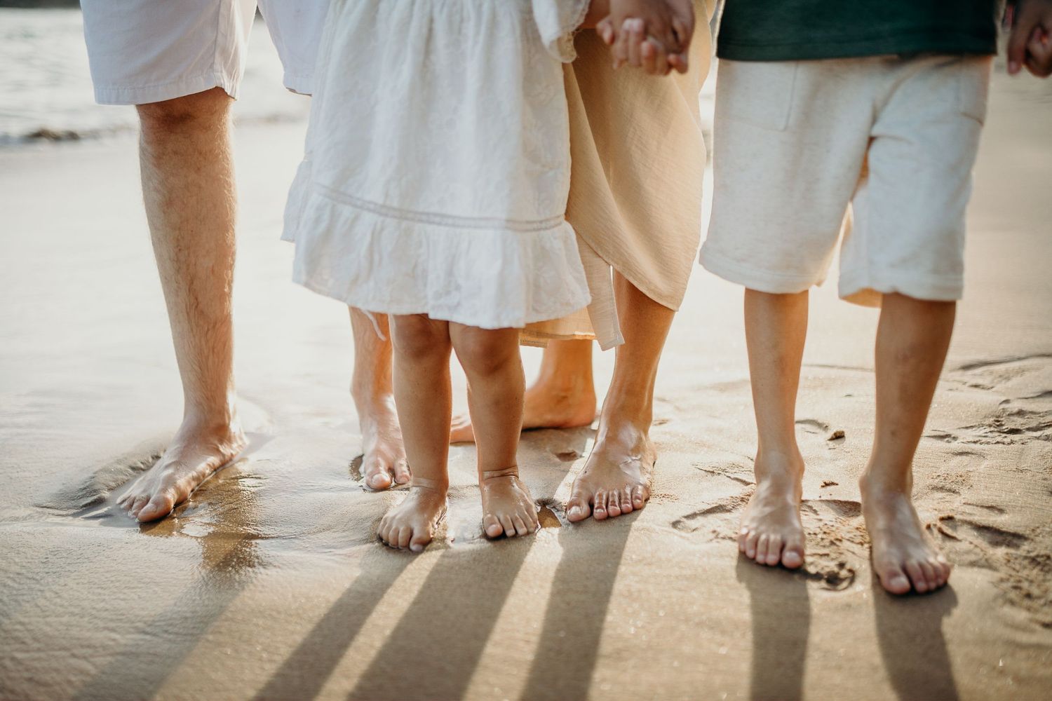 Close-up of family members' bare feet standing together on sandy beach.