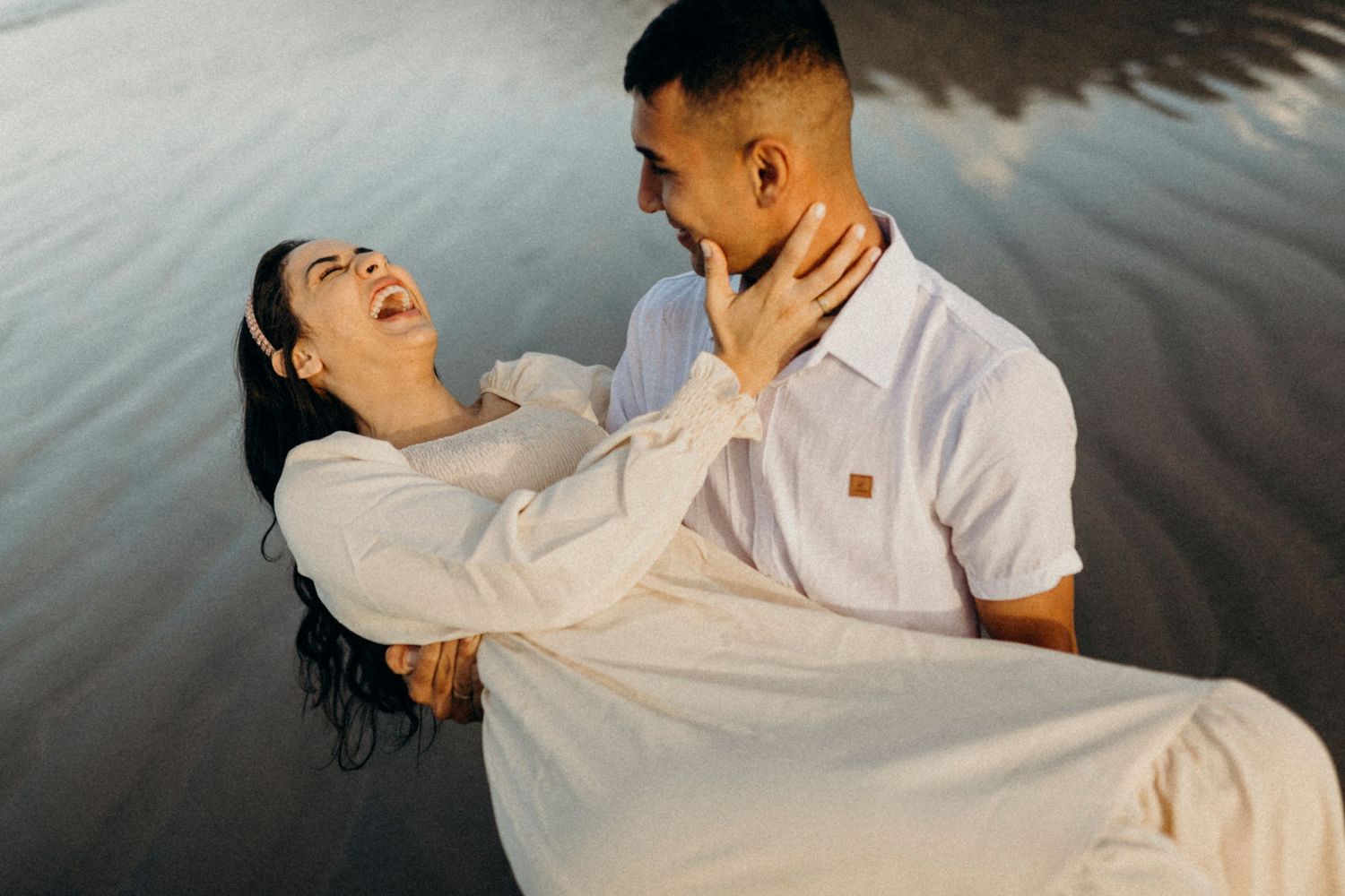 A loving couple shares an intimate dance-like pose while standing in shallow water at the beach.