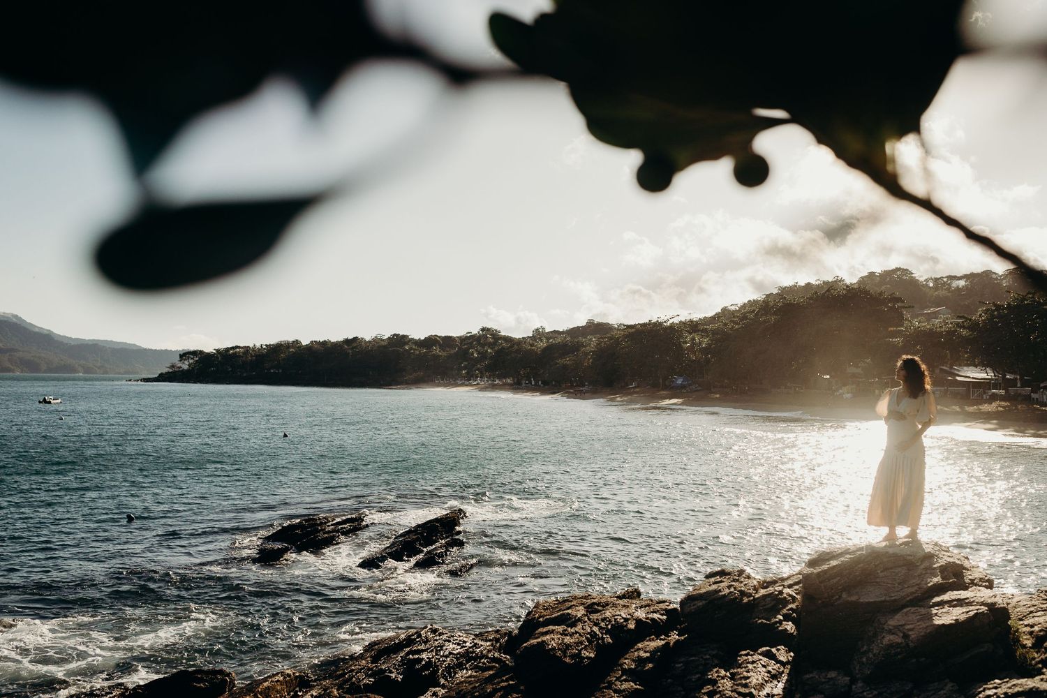 Silhouetted coastal landscape at sunset with dramatic lighting and ocean waves.