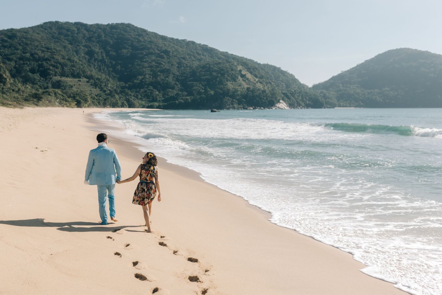 A couple walks hand in hand leaving footprints in the sand along a beautiful coastal beach.
