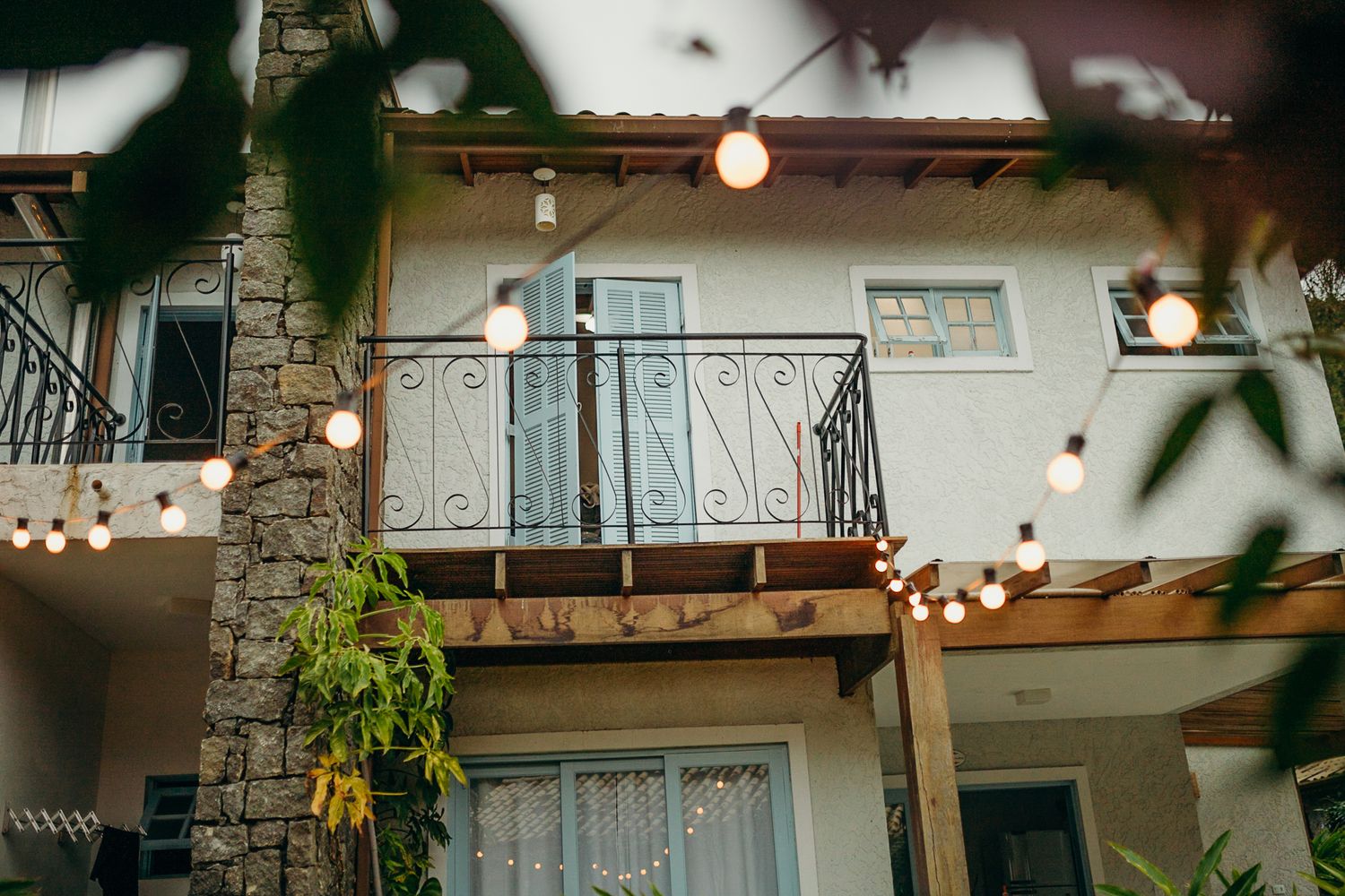 Stone and wood balcony with decorative iron railings illuminated by string lights.