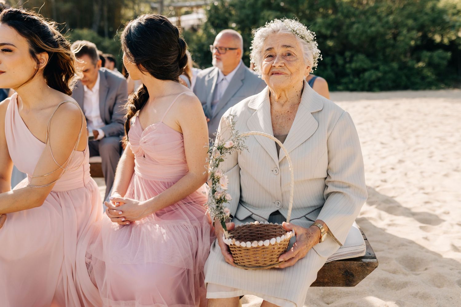 Wedding attendees in pink dresses seated at an outdoor ceremony.