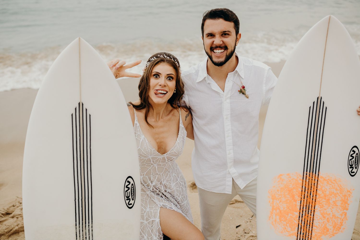 Newlyweds posing with surfboards on a tropical beach.