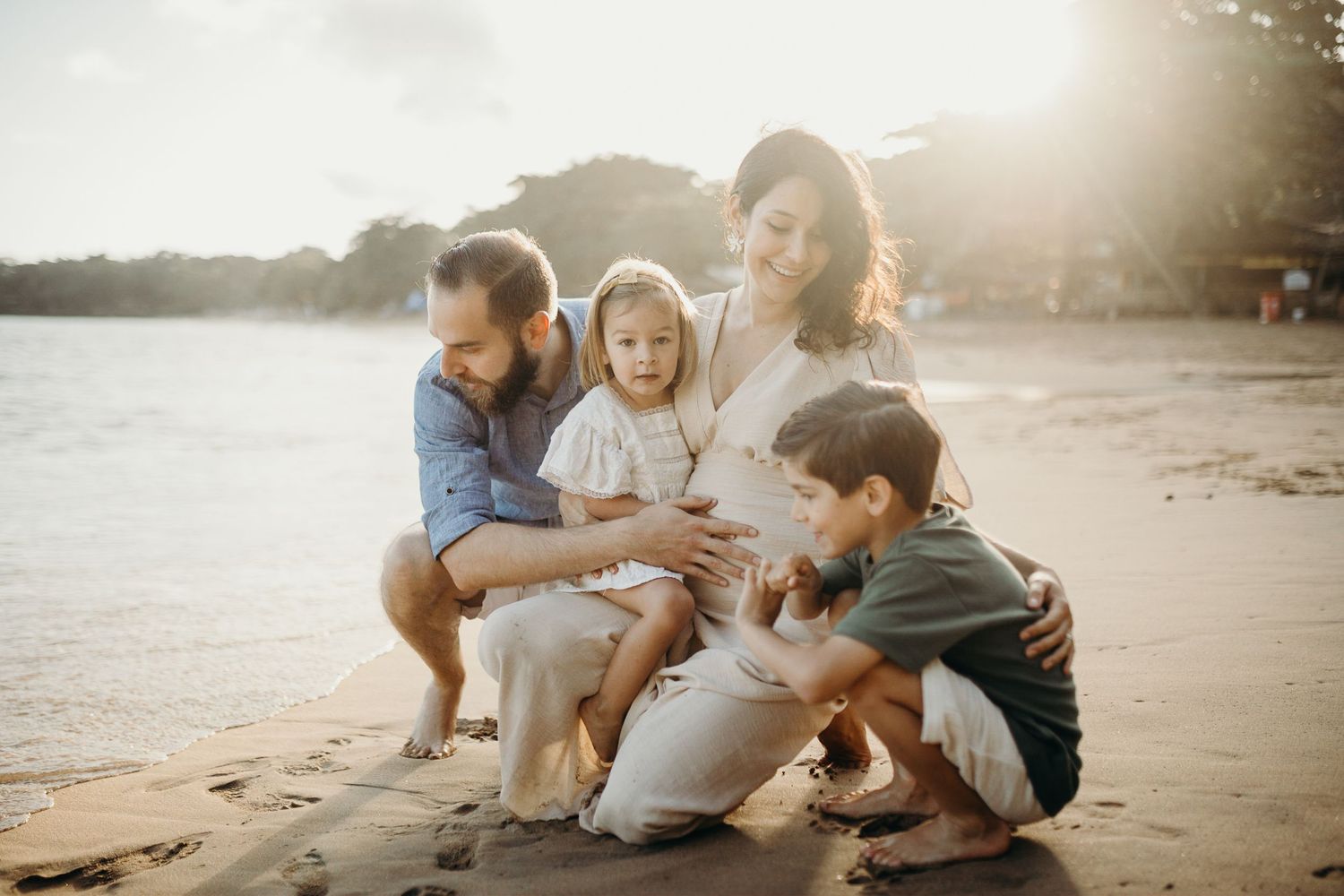 Dreamy beach photoshoot with family sitting together in golden light.