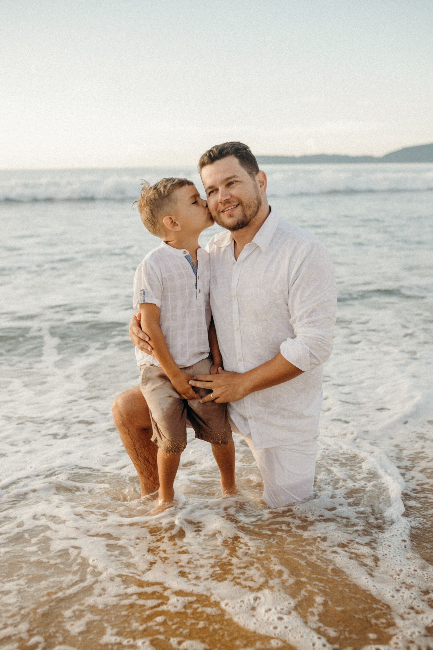 Heartwarming beach moment with parent and child standing in gentle surf.
