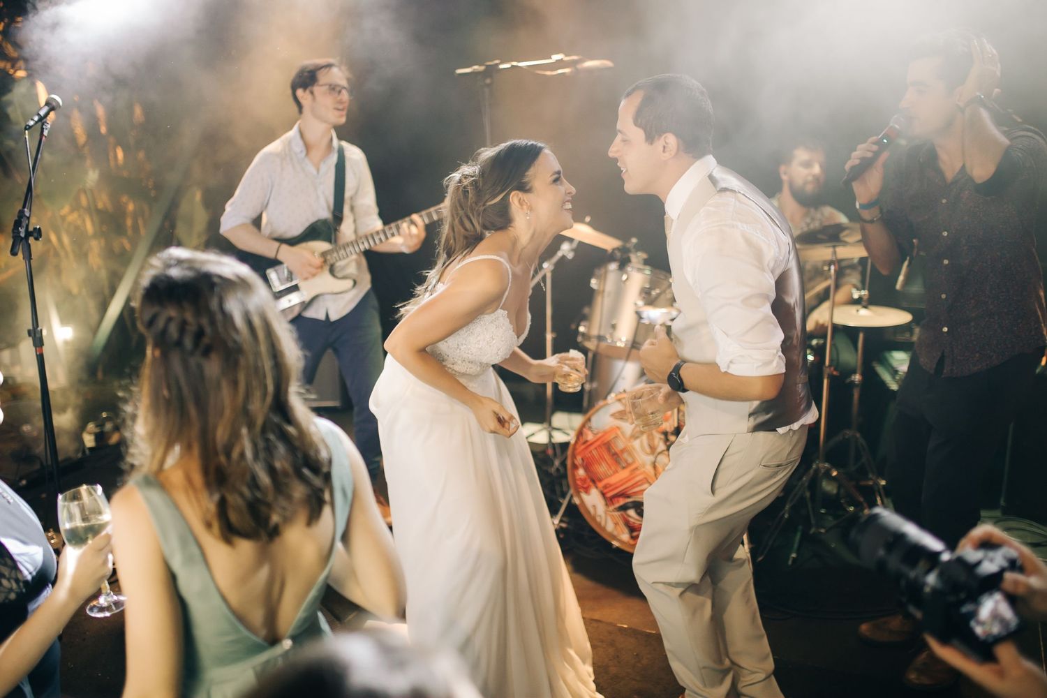 Couple dancing enthusiastically at their wedding reception with a live band performing behind them.