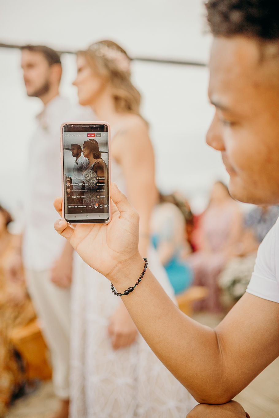 Wedding guests hold up cell phones to capture a special moment during an outdoor ceremony.
