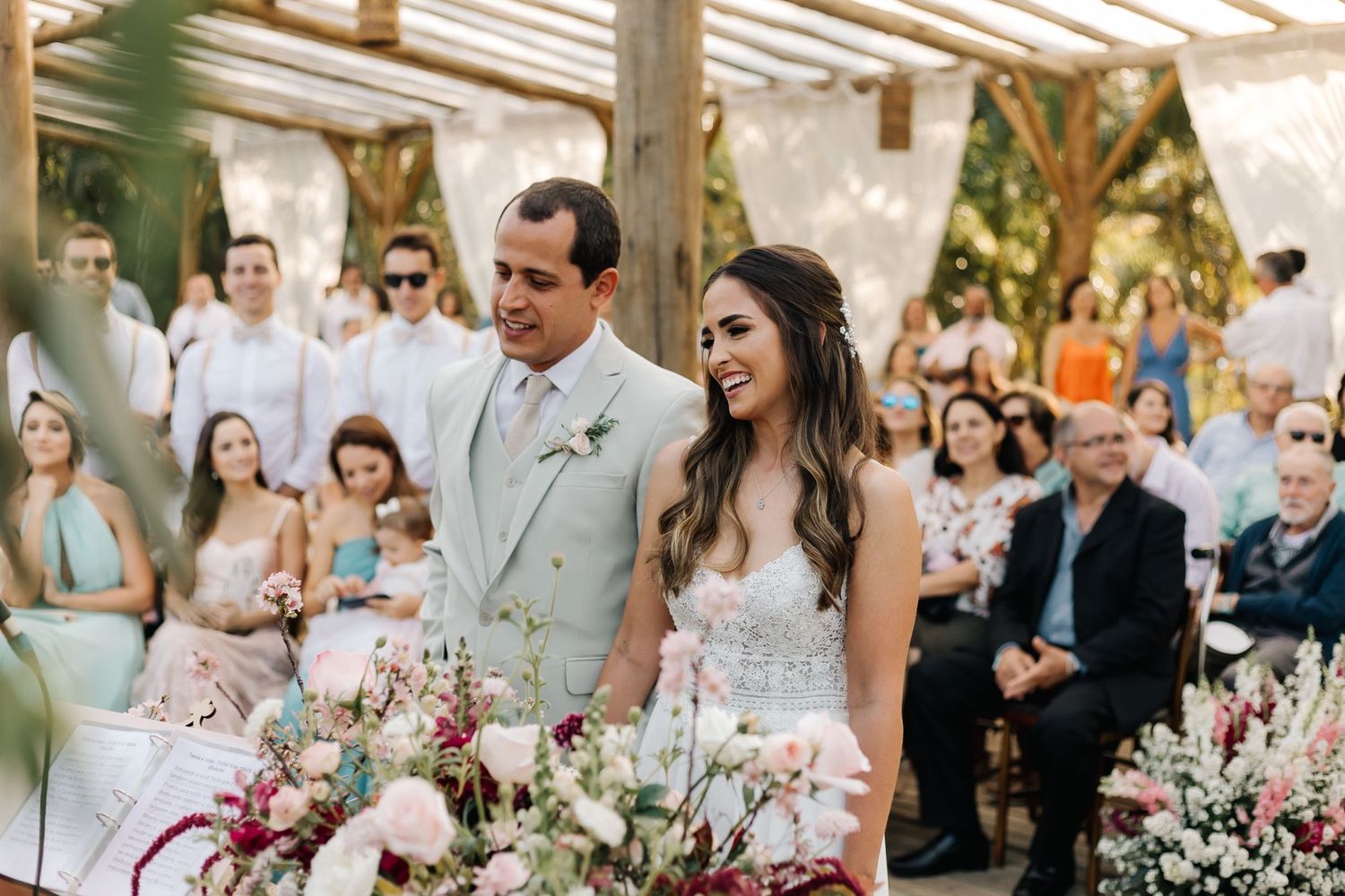 Elegant outdoor wedding ceremony with floral arrangements and wooden beams overhead.