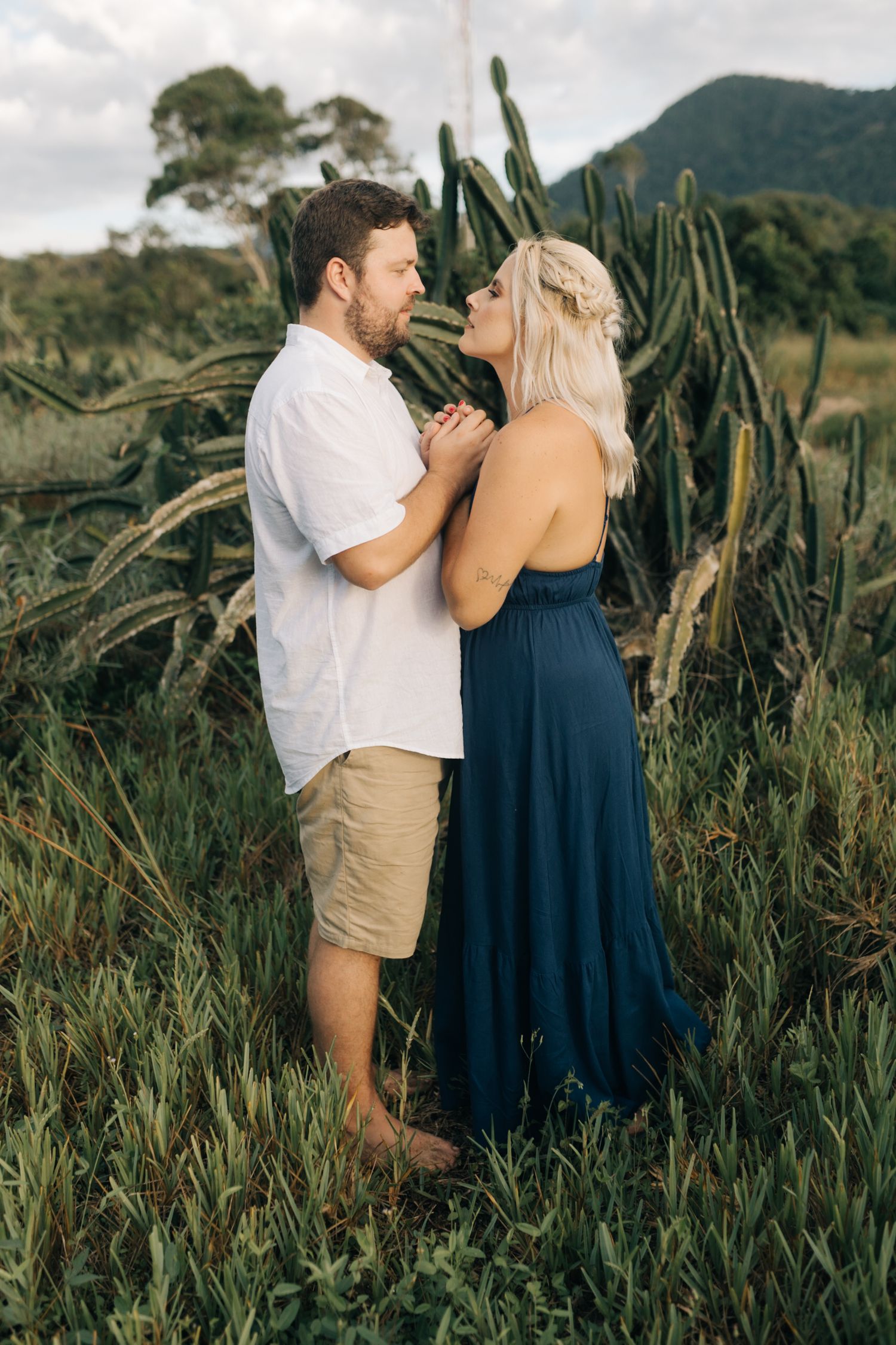 Romantic moment captured in tall grass with mountains and coastal scenery in the background.