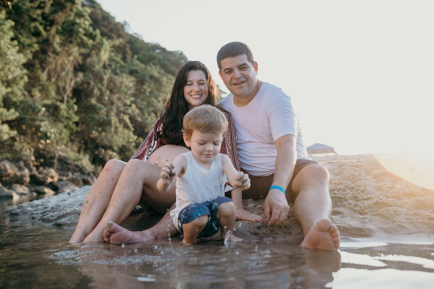 Family splashing and playing together in shallow water at sunset on a rocky beach.
