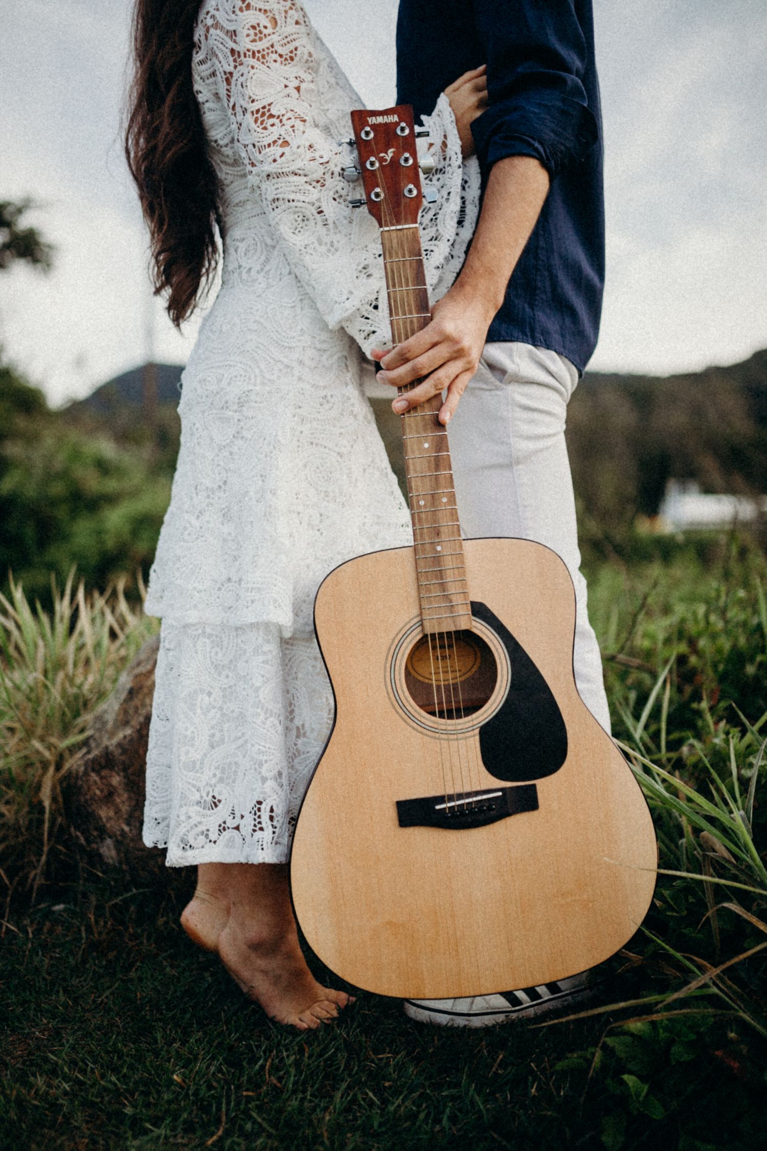 Detail shot of a couple holding an acoustic guitar while wearing contrasting navy and white outfits.