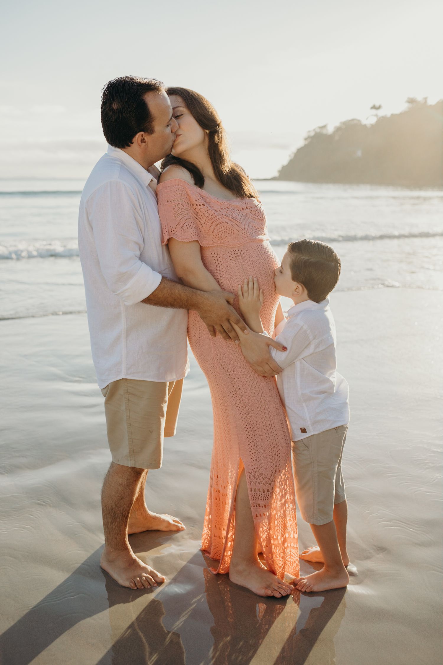 Family shares loving moments together on a sandy beach at sunset with waves in the background.