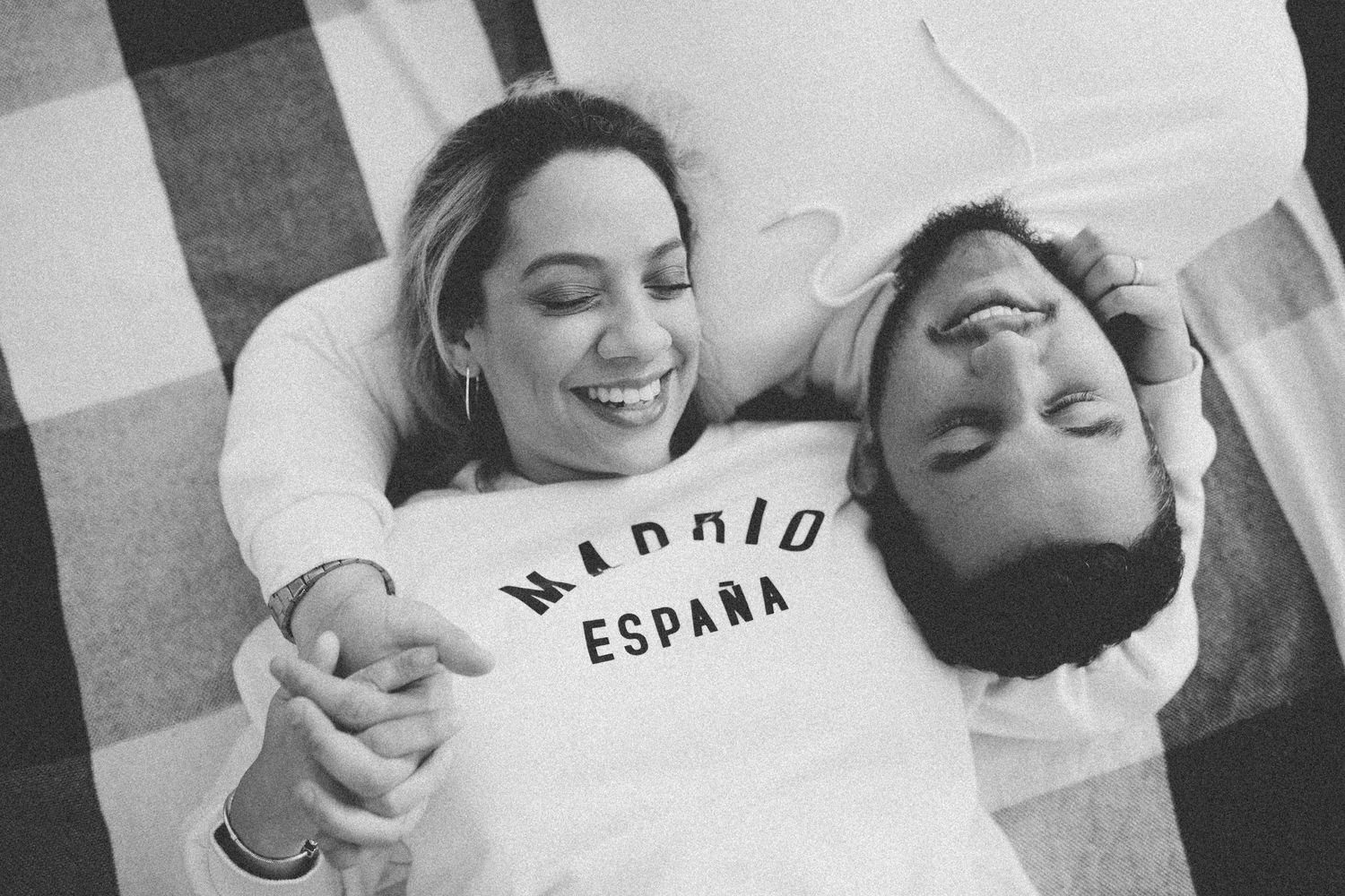 Black and white shot of couple smiling while lying on plaid blanket.