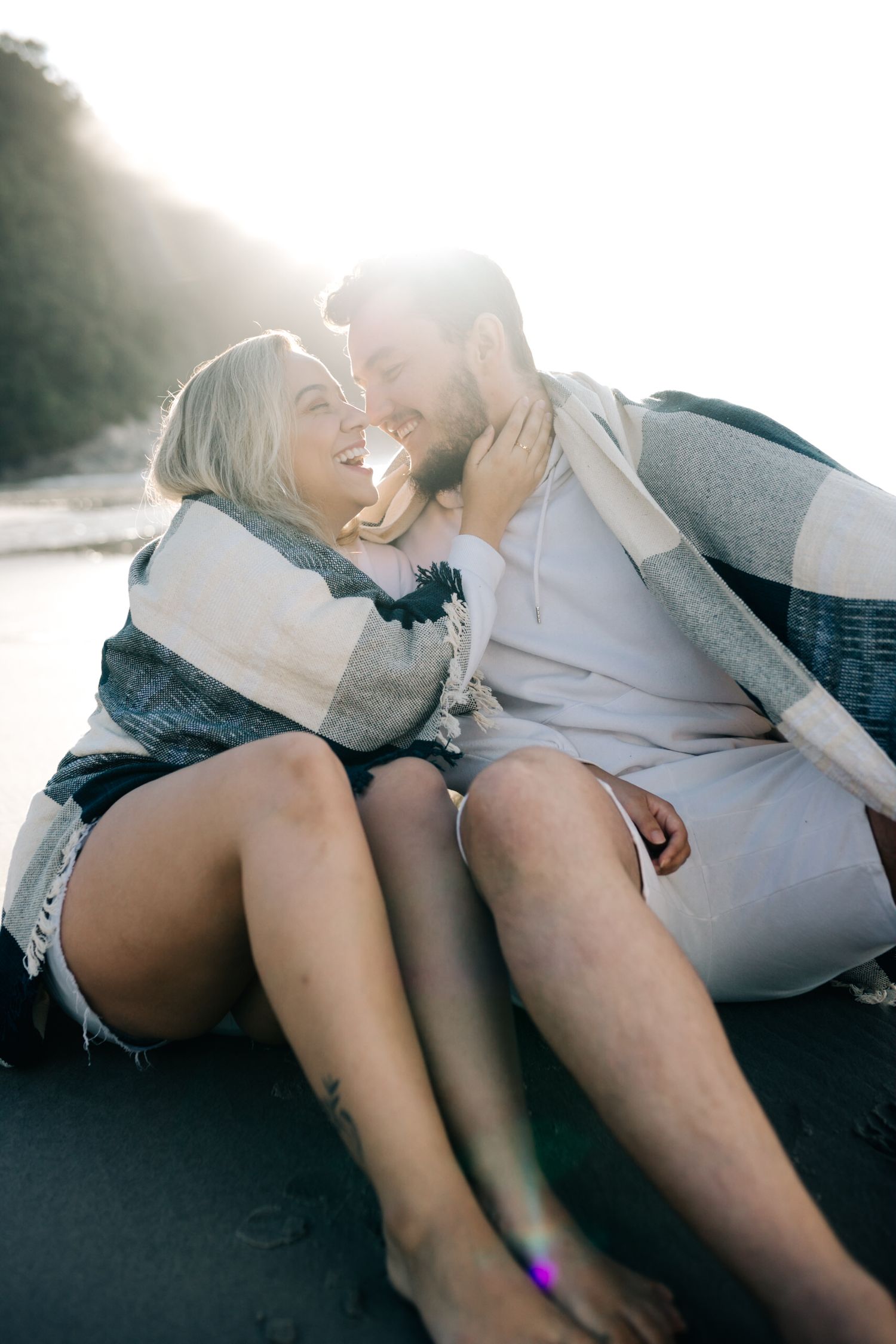 Intimate couple sharing romantic moment on beach at sunset wrapped in blanket.