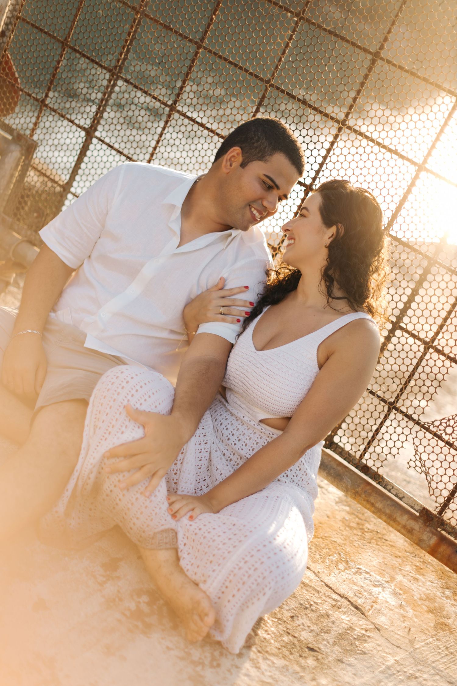 Romantic couple in white attire pose against geometric backdrop during golden hour.