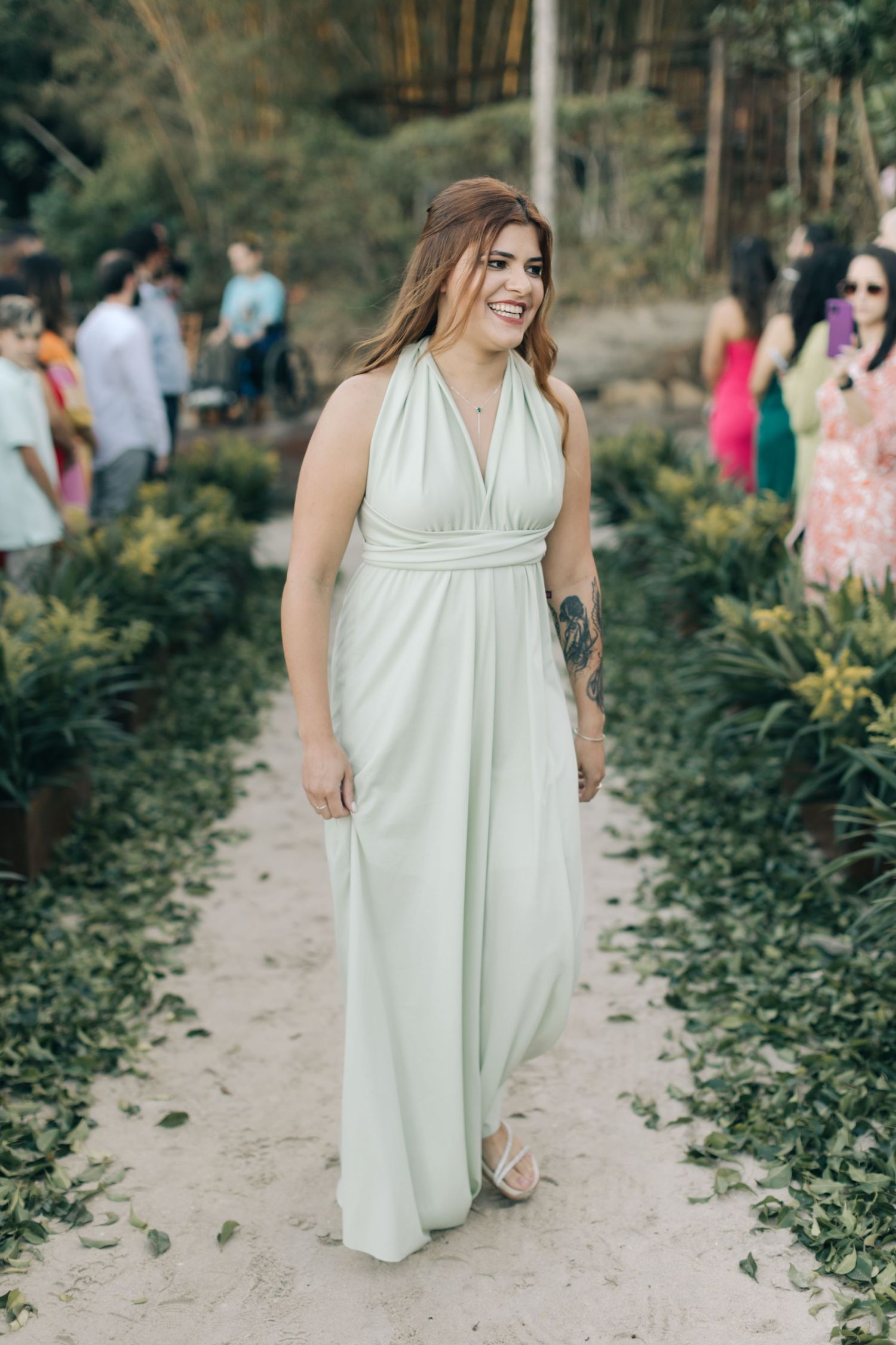 A bridesmaid walks down a garden path wearing a flowing cream-colored gown.