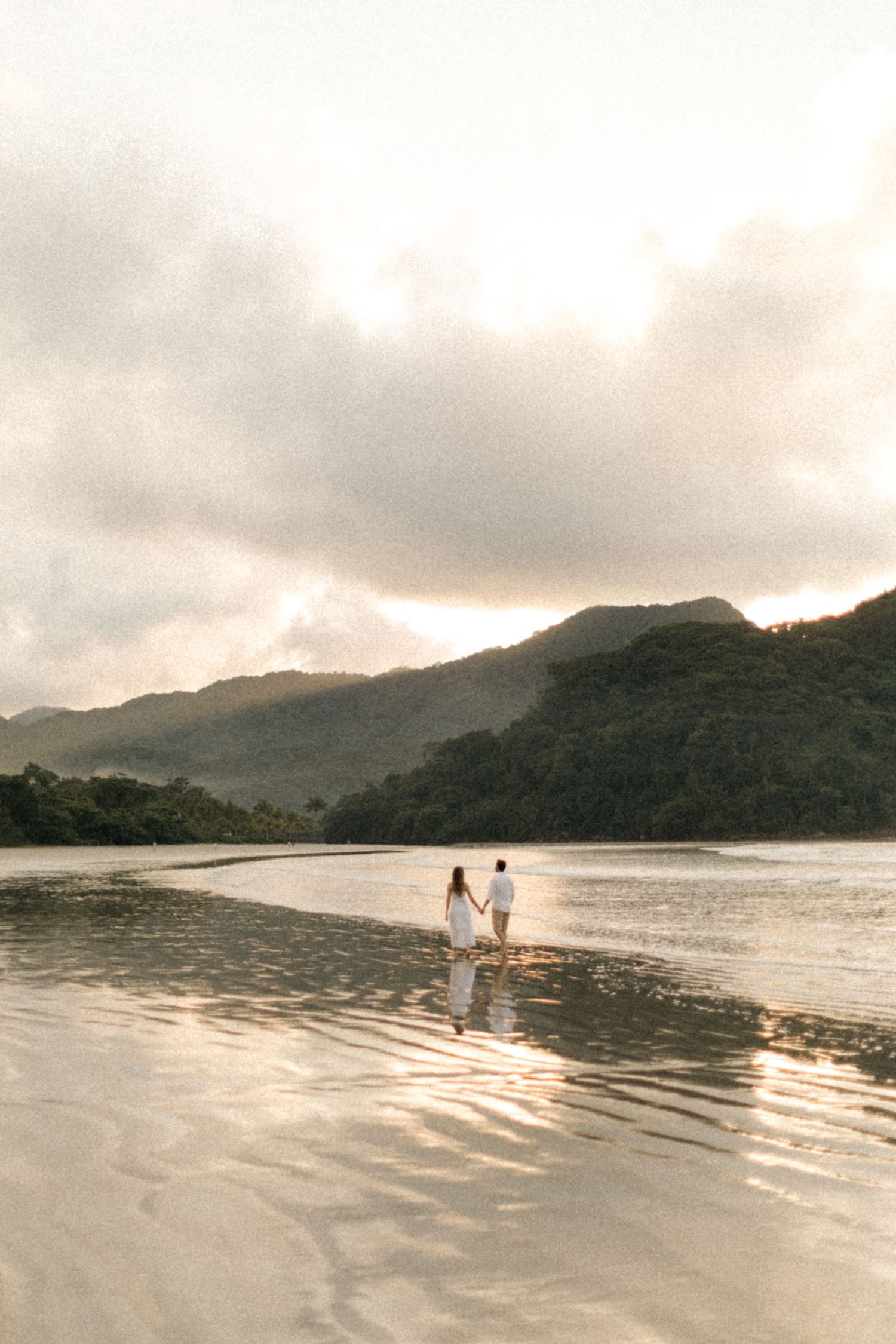 Wide angle shot of a beach landscape with mountains and two distant figures walking along the shore.