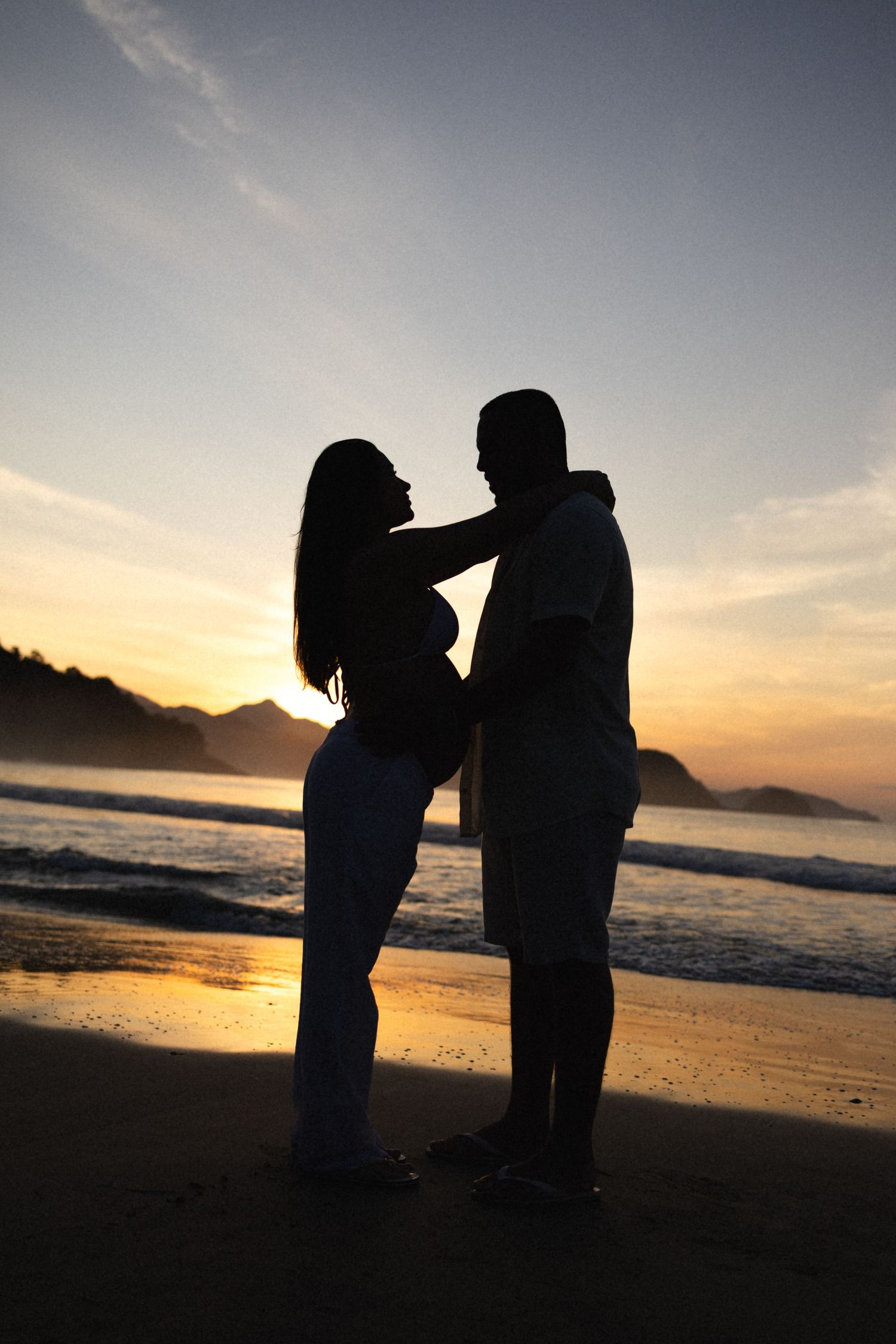Silhouetted couple stands together on beach against stunning sunset backdrop.