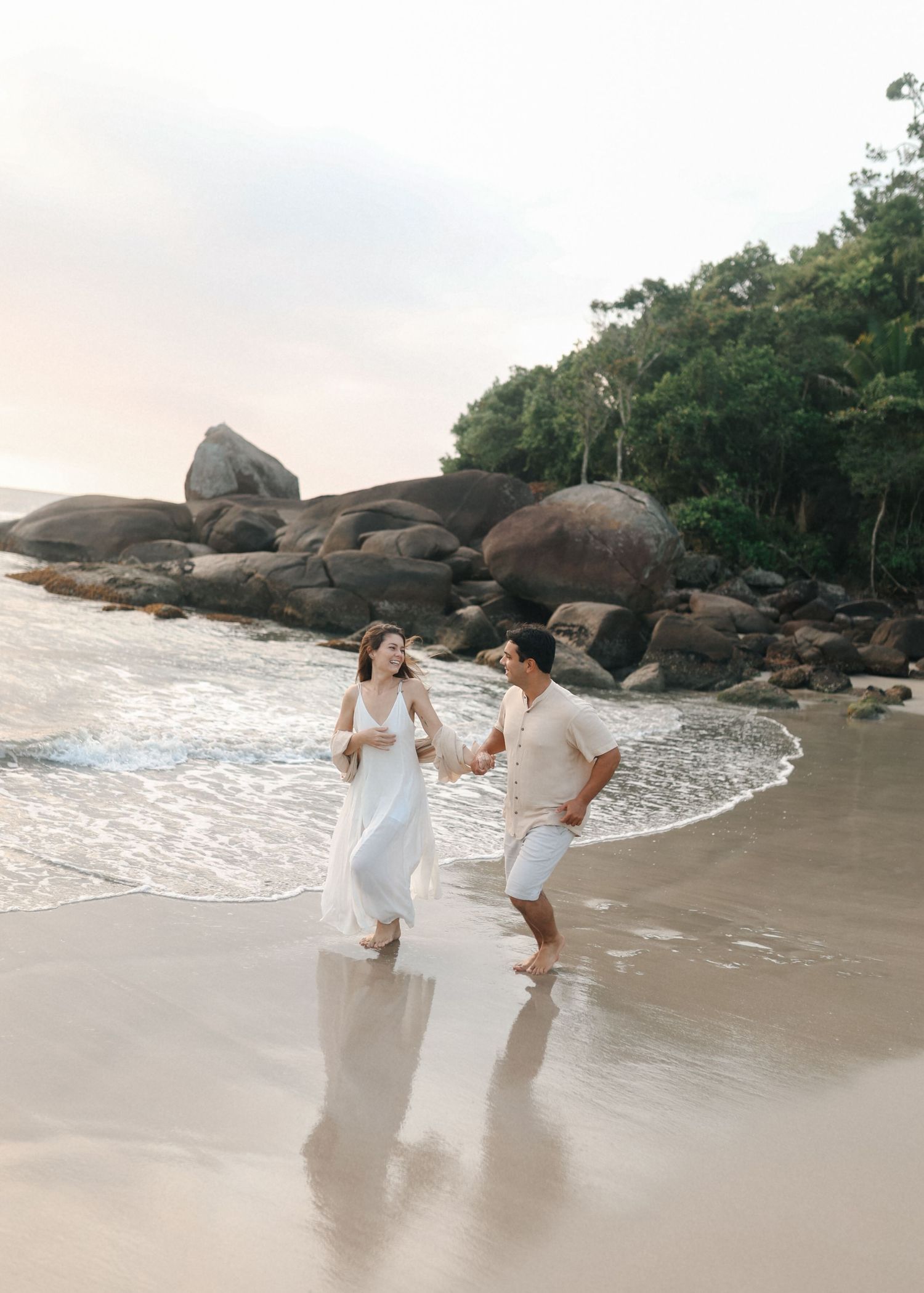 Playful couple splashes in ocean waves during beach sunset photography session.