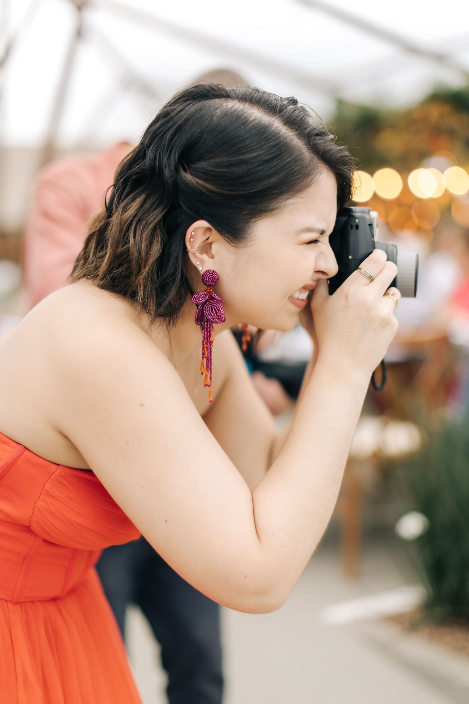 Wedding guest in orange dress takes photos with vintage camera at reception.