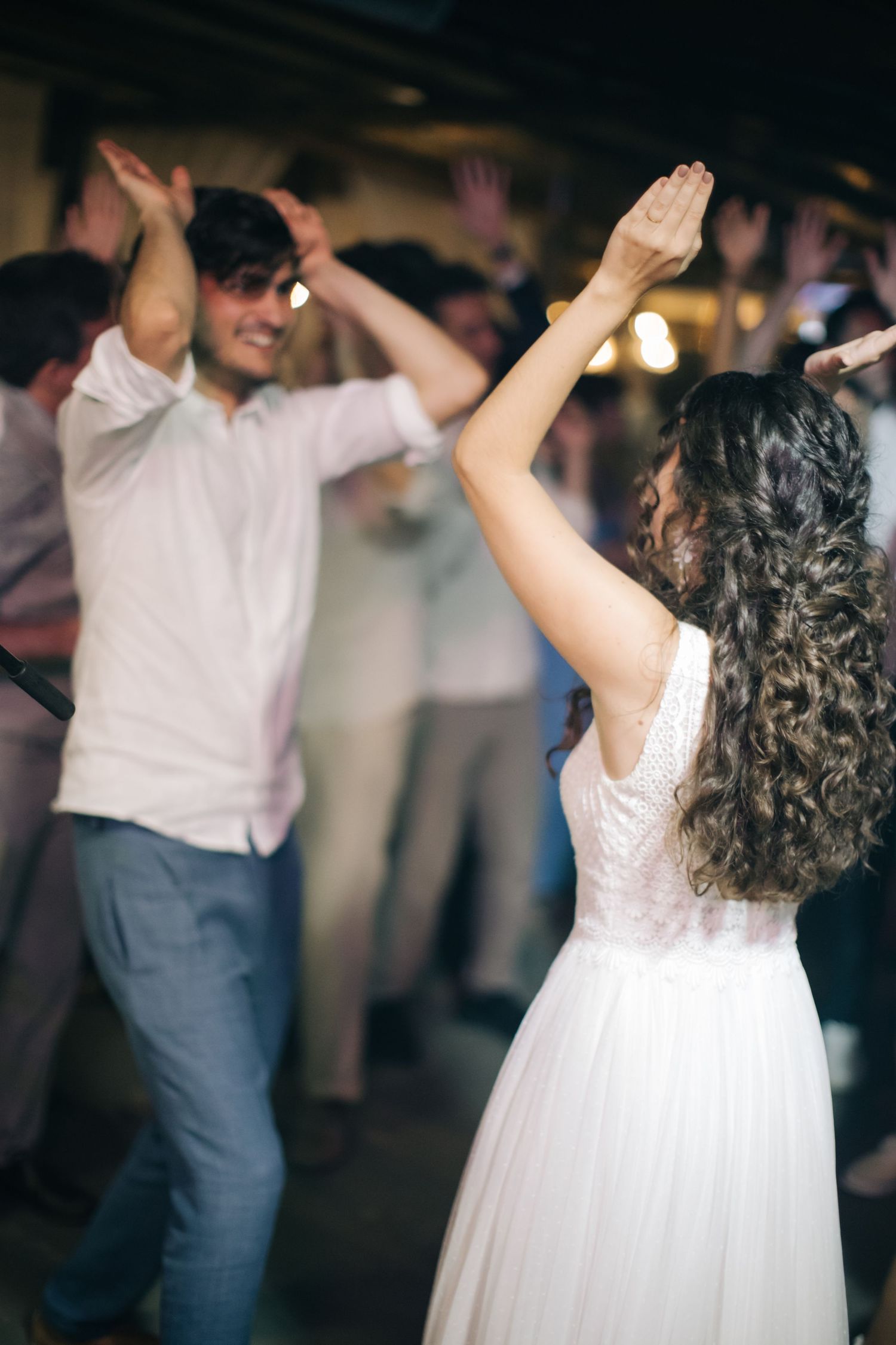 A couple dancing with raised arms at their wedding reception, captured in candid motion.