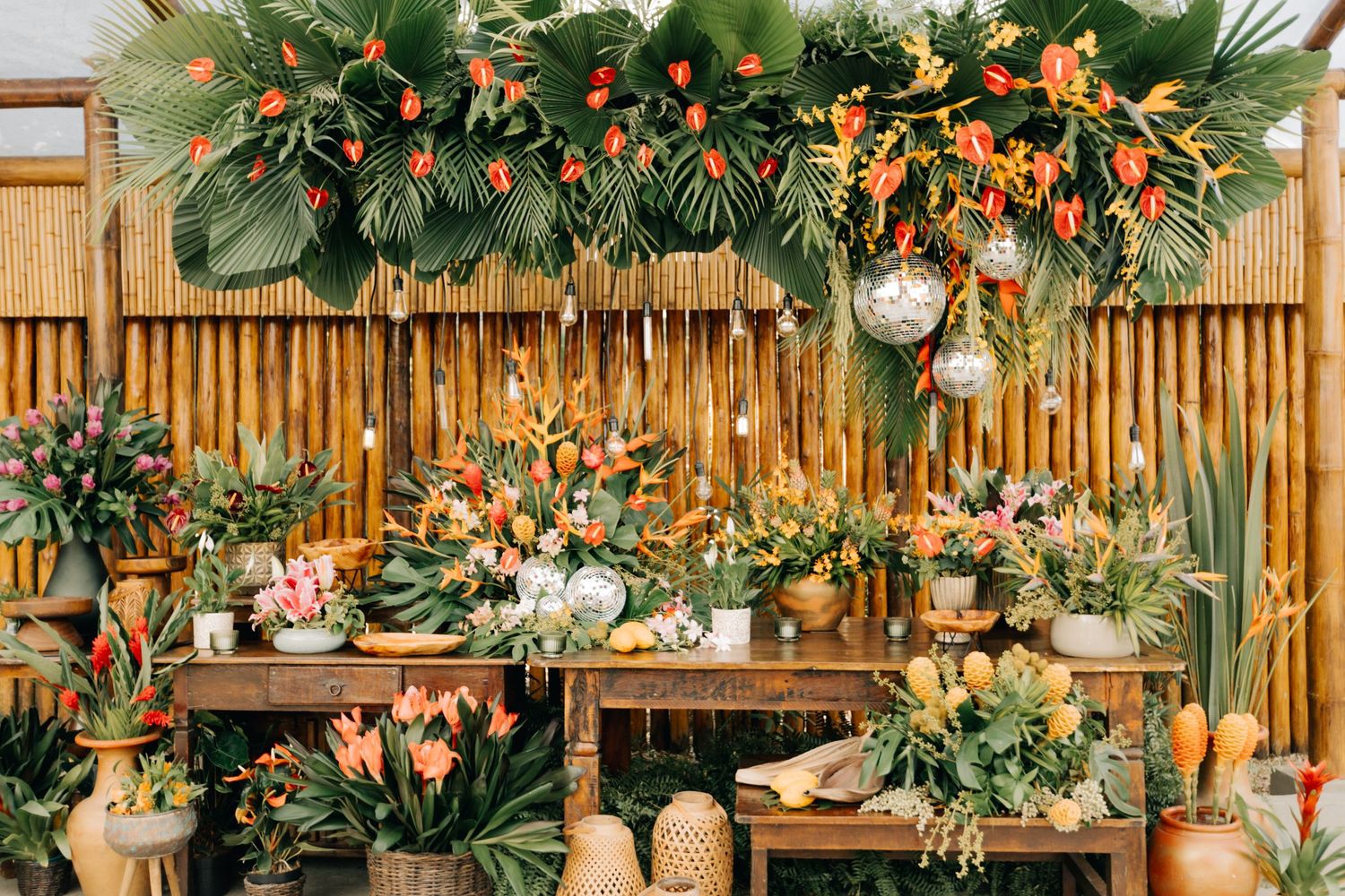Rustic wooden display table decorated with tropical foliage and orange flowers against bamboo wall.