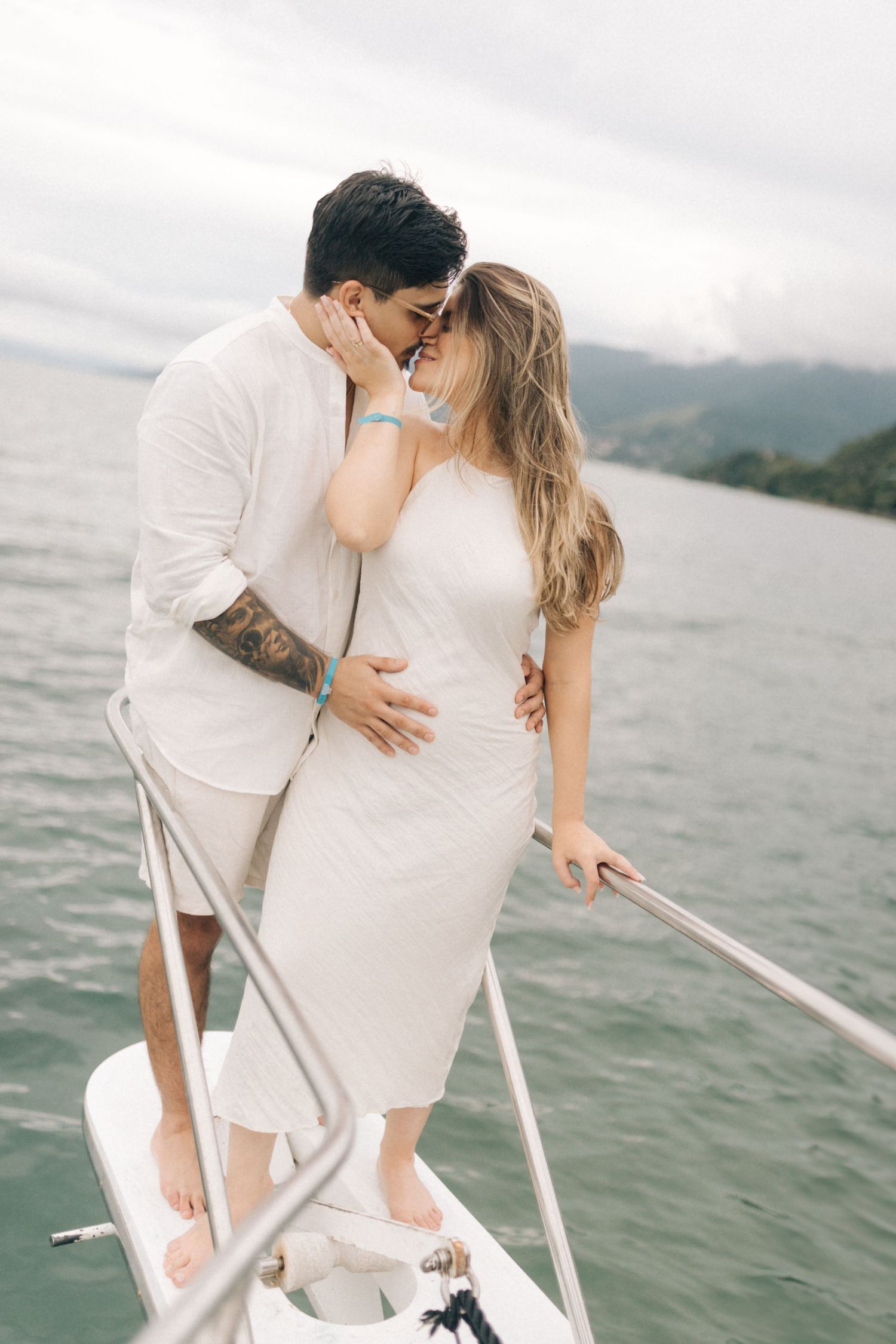 Intimate moment captured between couple in white clothing on boat with scenic mountain backdrop.