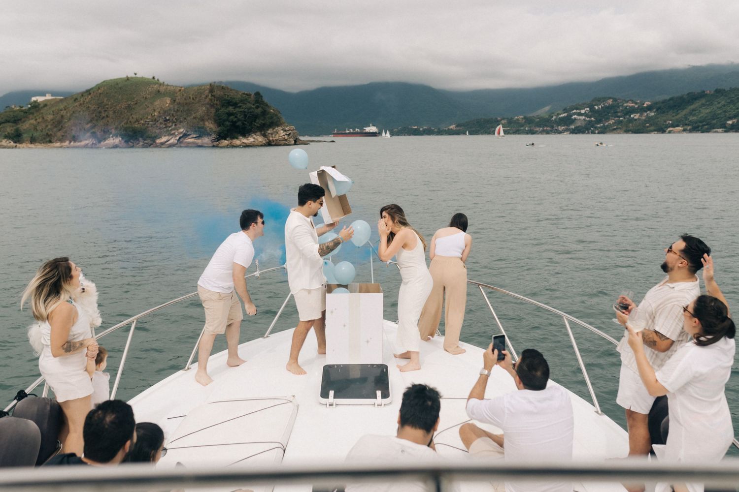 White yacht deck with passengers relaxing against scenic mountain bay backdrop.
