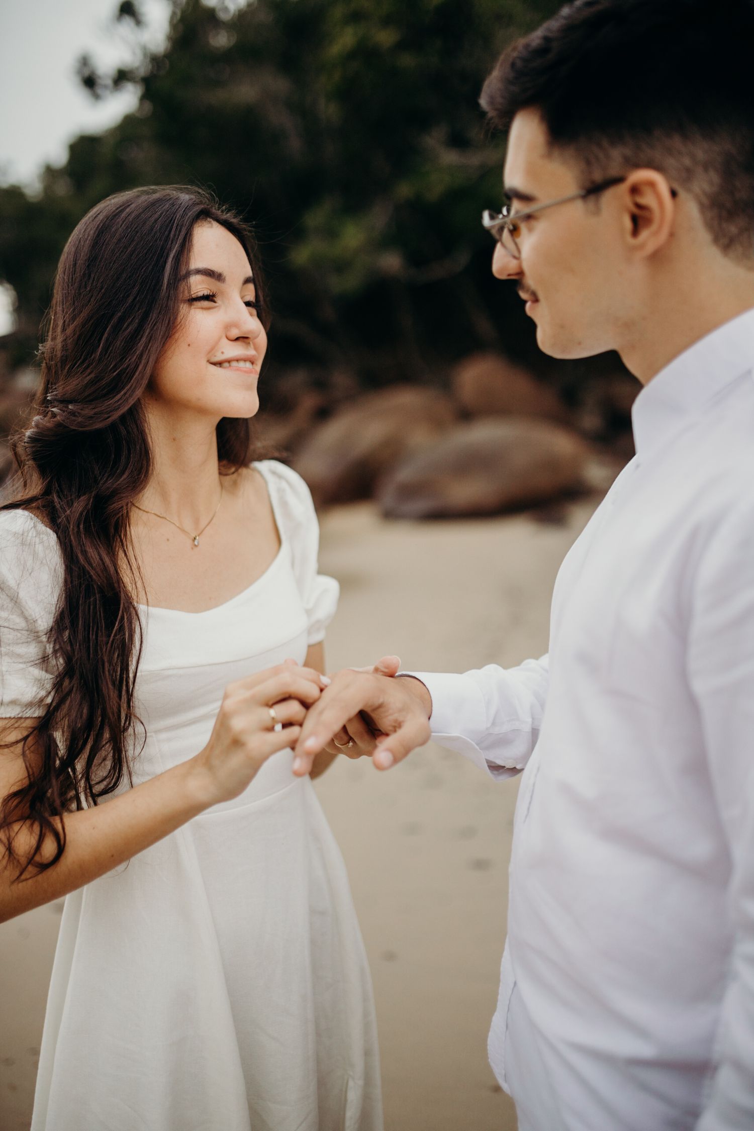 A romantic couple in white outfits dances together on a secluded beach.