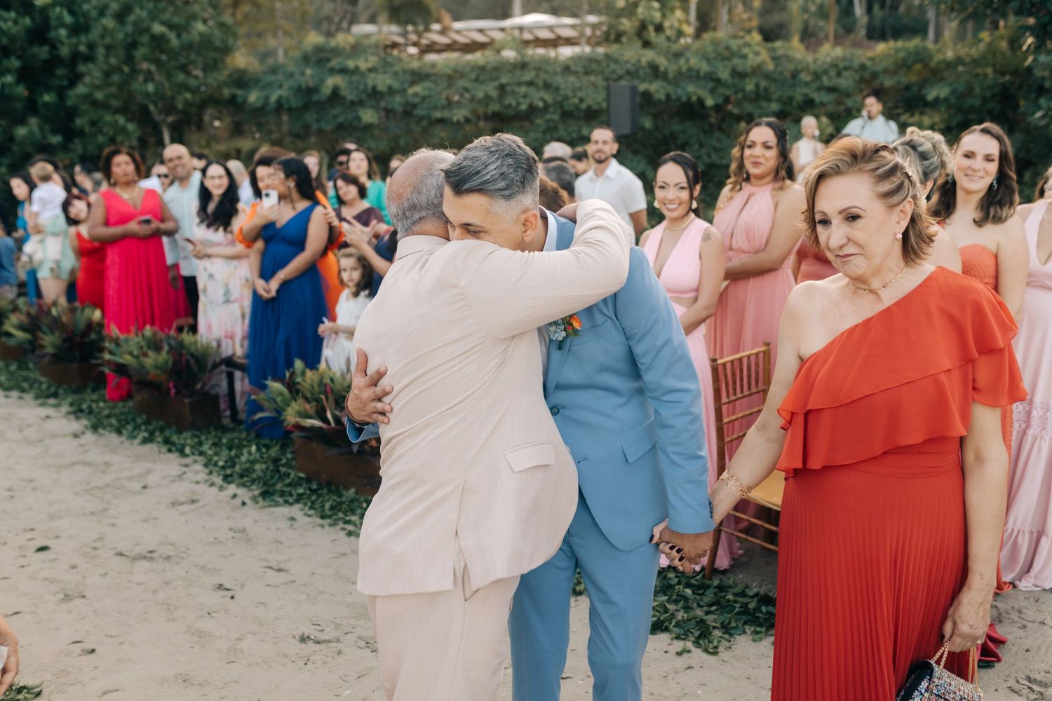 Wedding celebration moment with guests in colorful dresses gathered along a garden path.