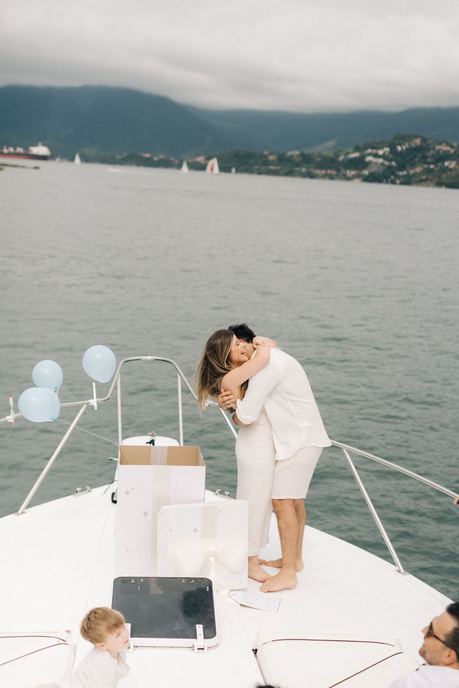 A romantic moment captured on a yacht's bow with mountains and water in the background.