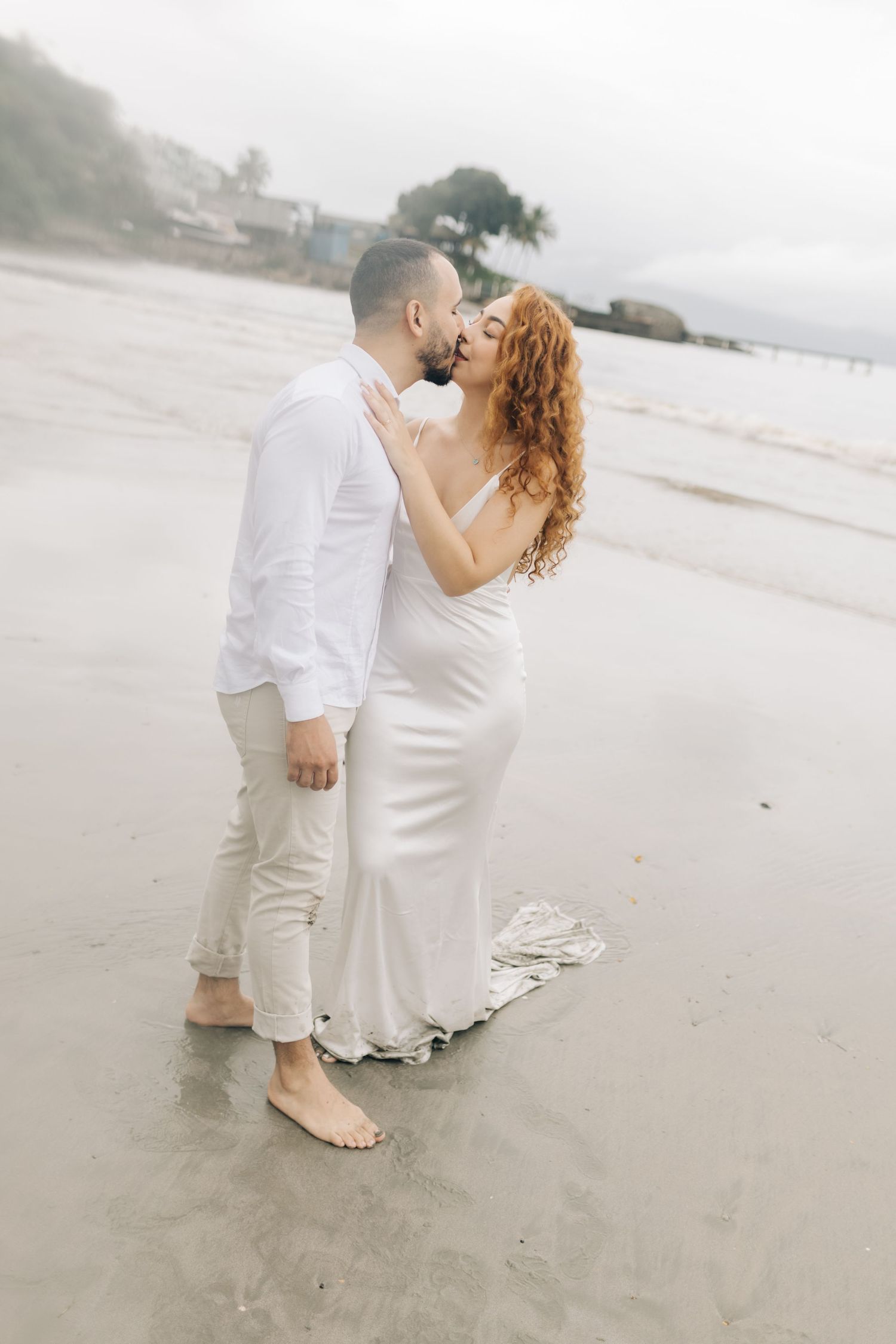 A romantic beach moment captured as a couple in white embraces on the sandy shore.