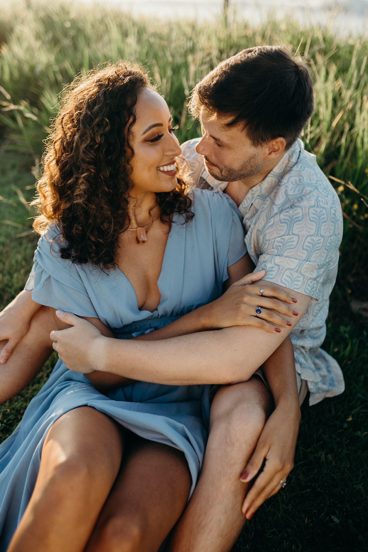 Affectionate couple in casual summer attire embracing in sunlit meadow.