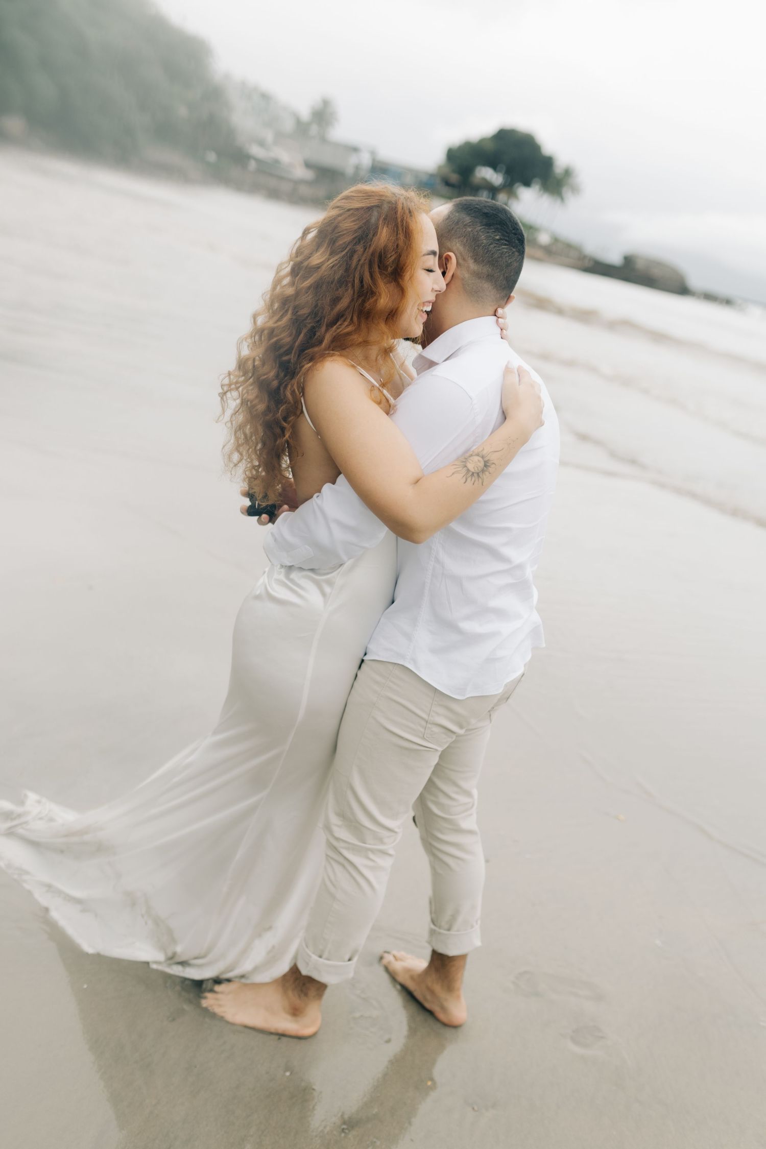 A romantic beach photoshoot features a couple in white attire sharing an intimate moment.