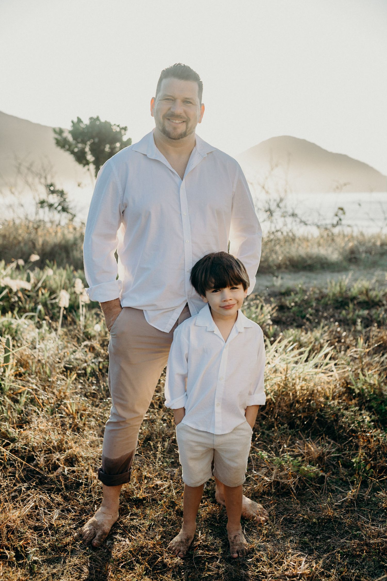 A parent and child stand together on a scenic hillside during sunset.