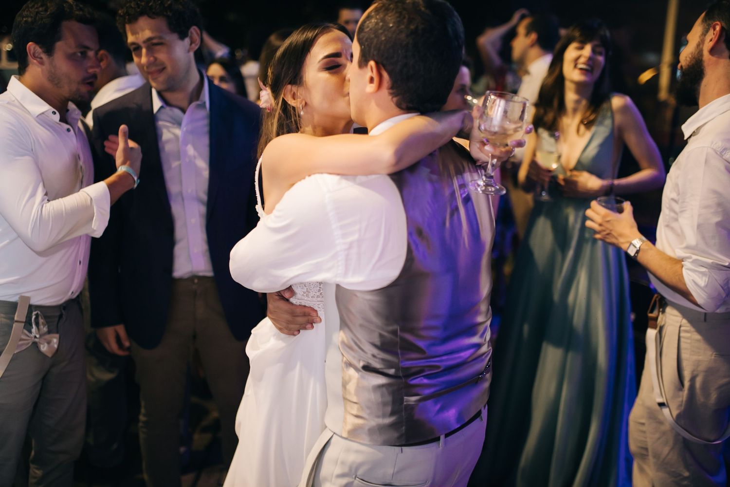 Intimate slow dance moment during evening wedding reception with guests in background.