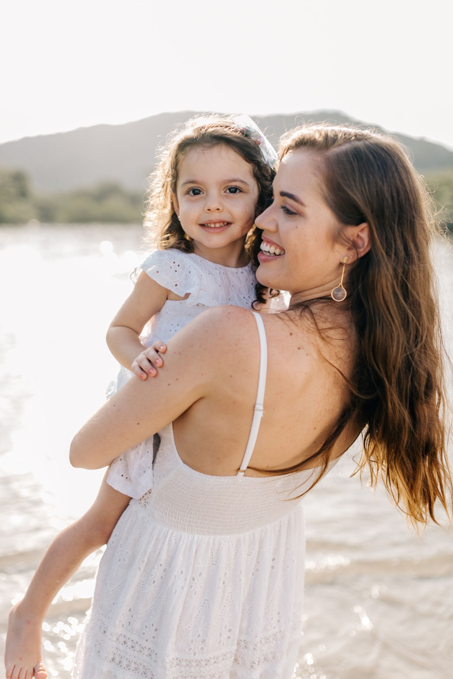 A tender embrace between parent and child on a sunny beach with mountains in the background.