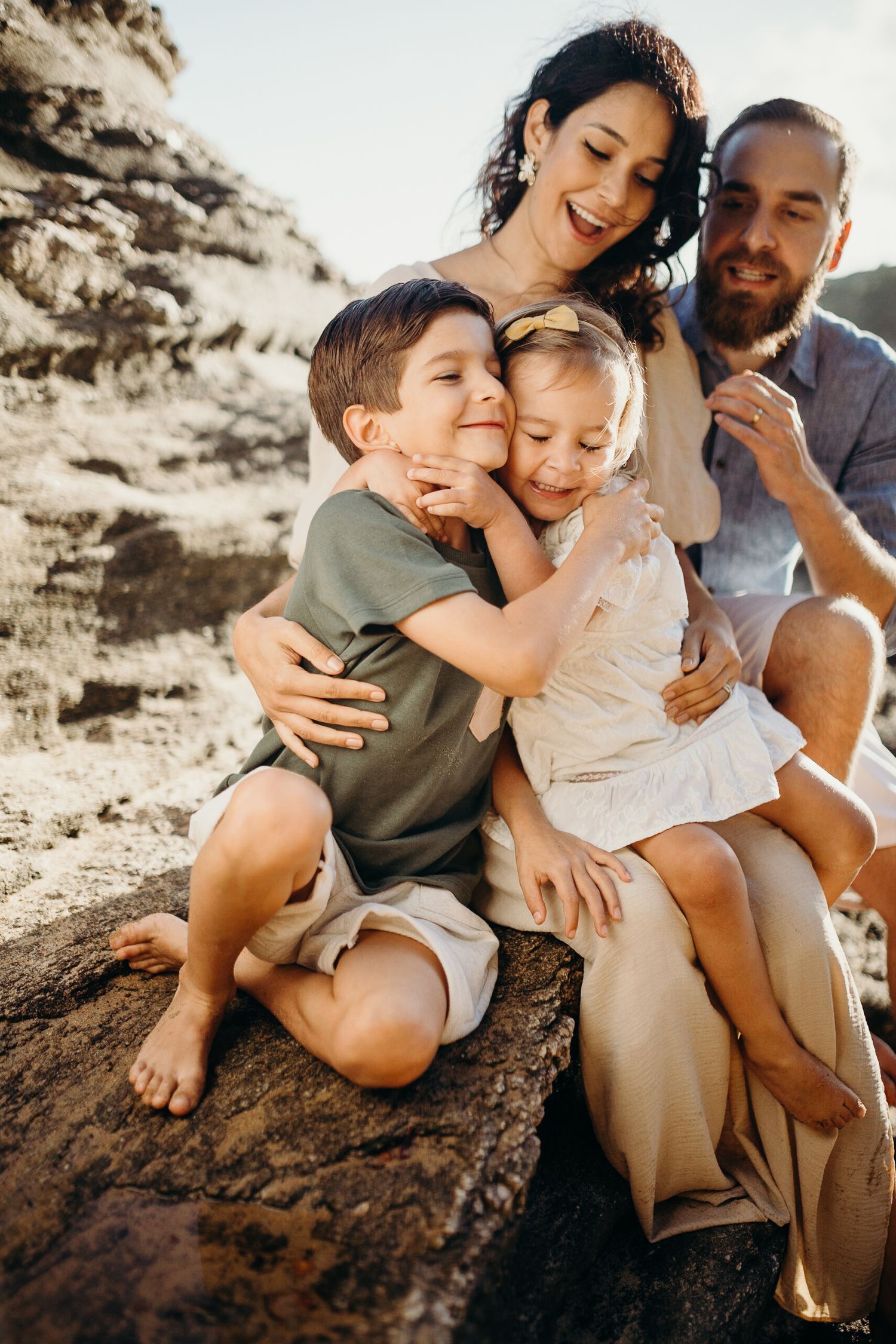A playful family embrace captured on rocky coastal terrain during sunset.