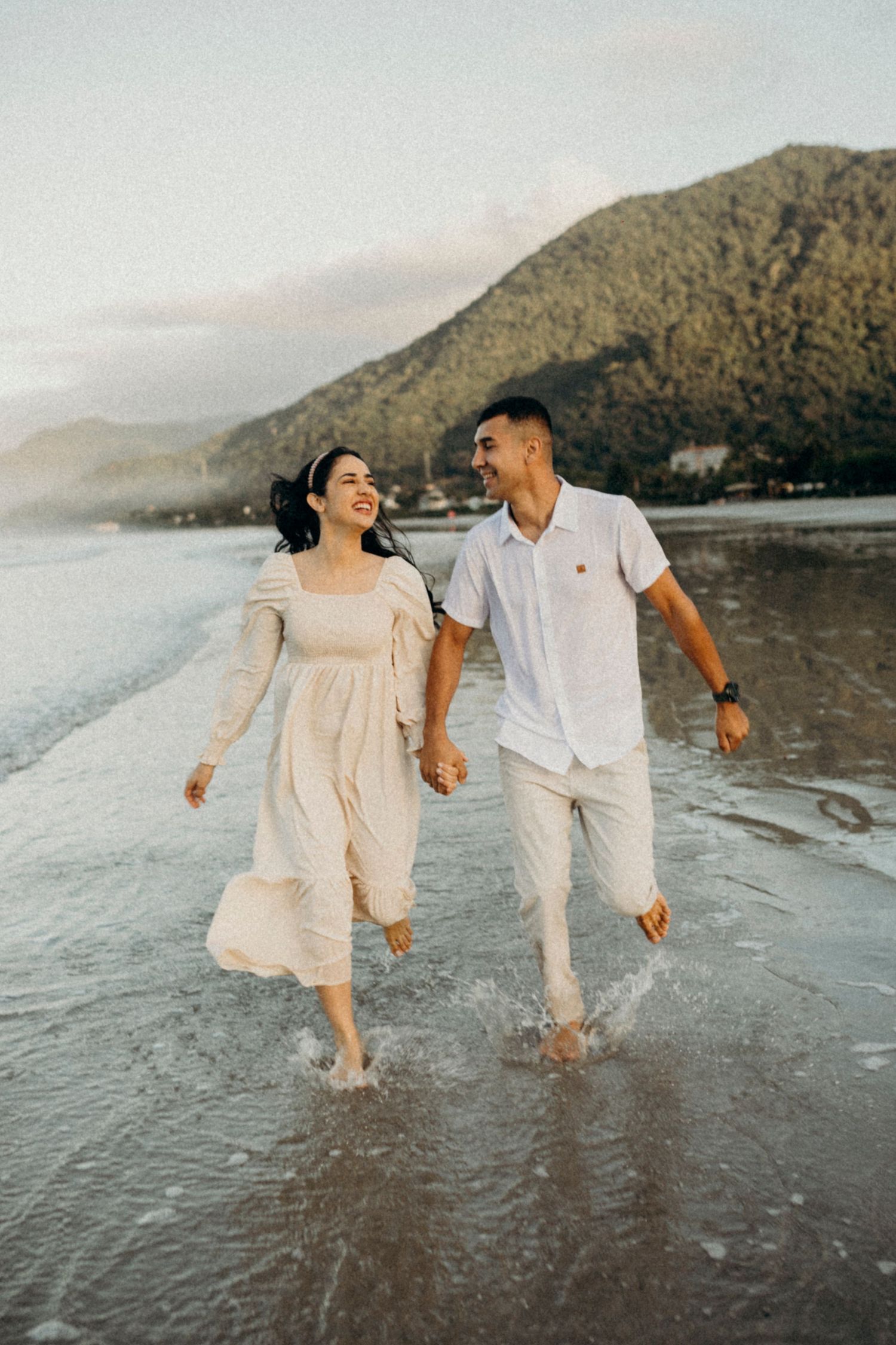 Couple walking hand in hand along the shoreline at sunset wearing coordinated beach outfits.