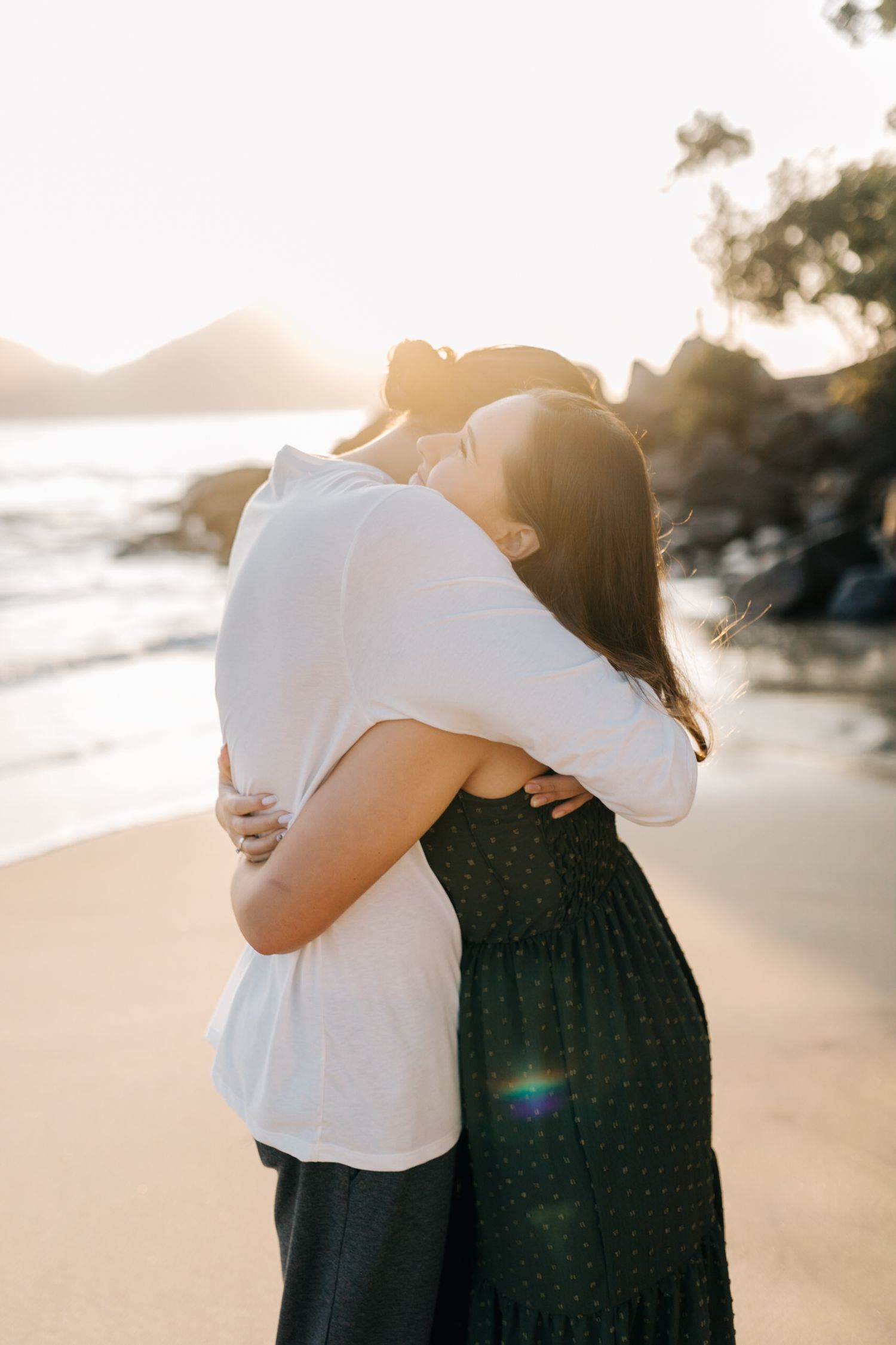 Sunset beach embrace with soft natural lighting and coastal rocks.