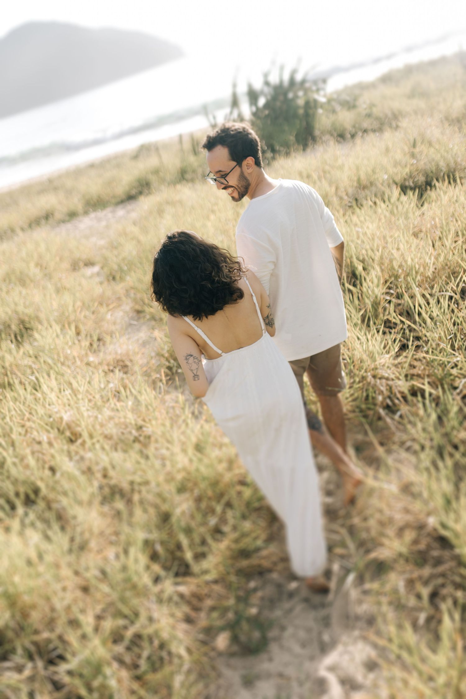 Couple walking down a grassy coastal path in white summer outfits.