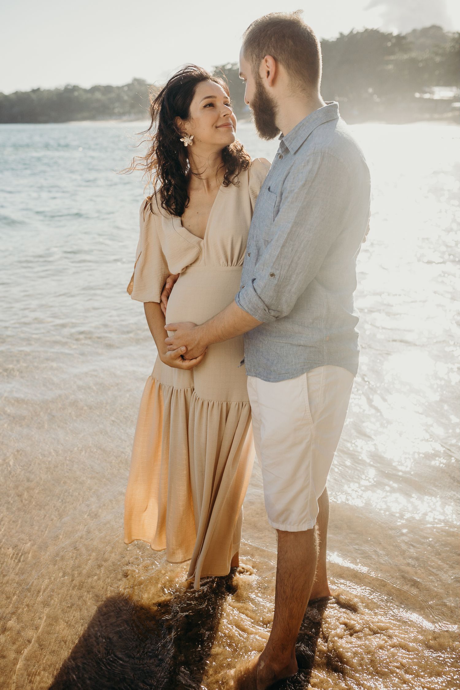 A romantic maternity photoshoot captured against ocean waves and rocky coastline.