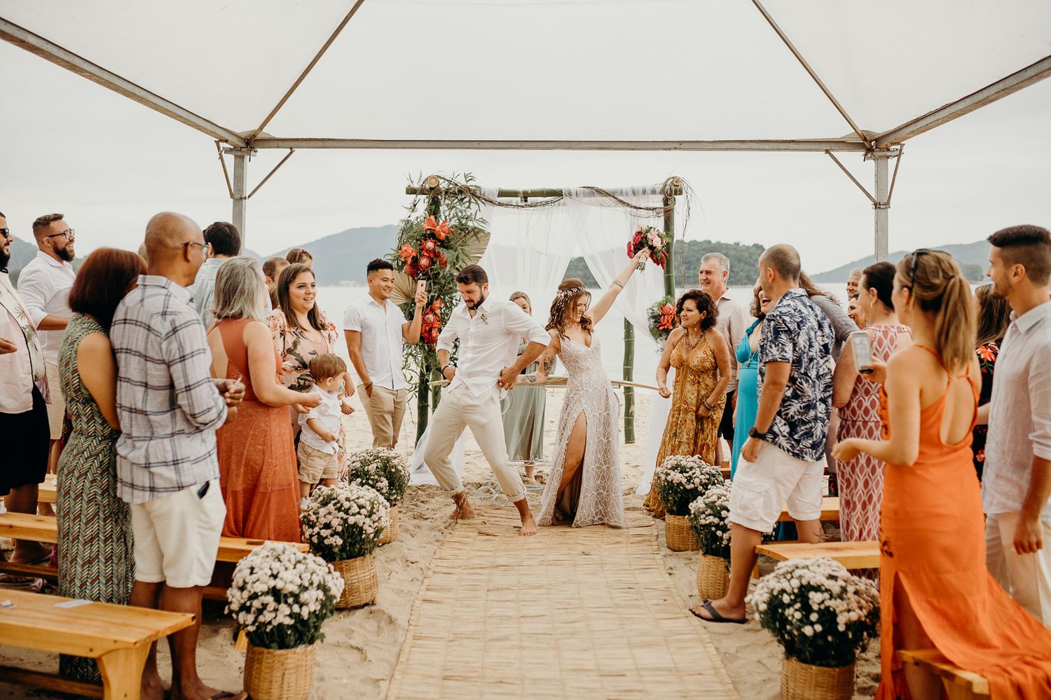 A beachfront wedding ceremony under a white tent decorated with floral arrangements.