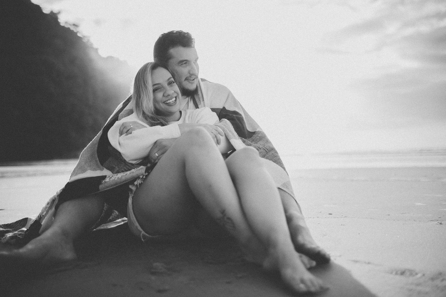 A candid black and white photo of a couple laughing together on the beach.