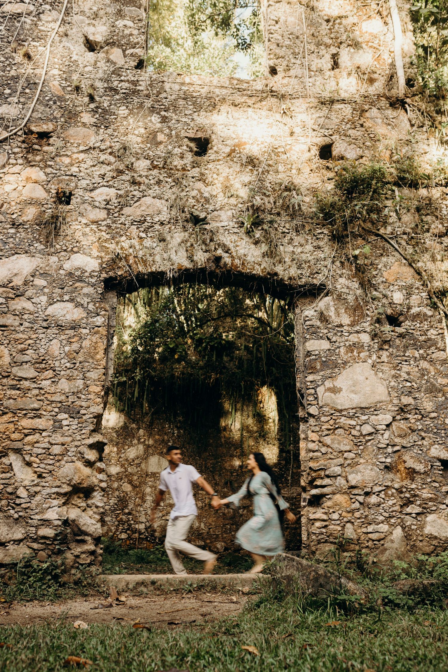 A couple twirls playfully through an ancient stone archway in a historic ruin.
