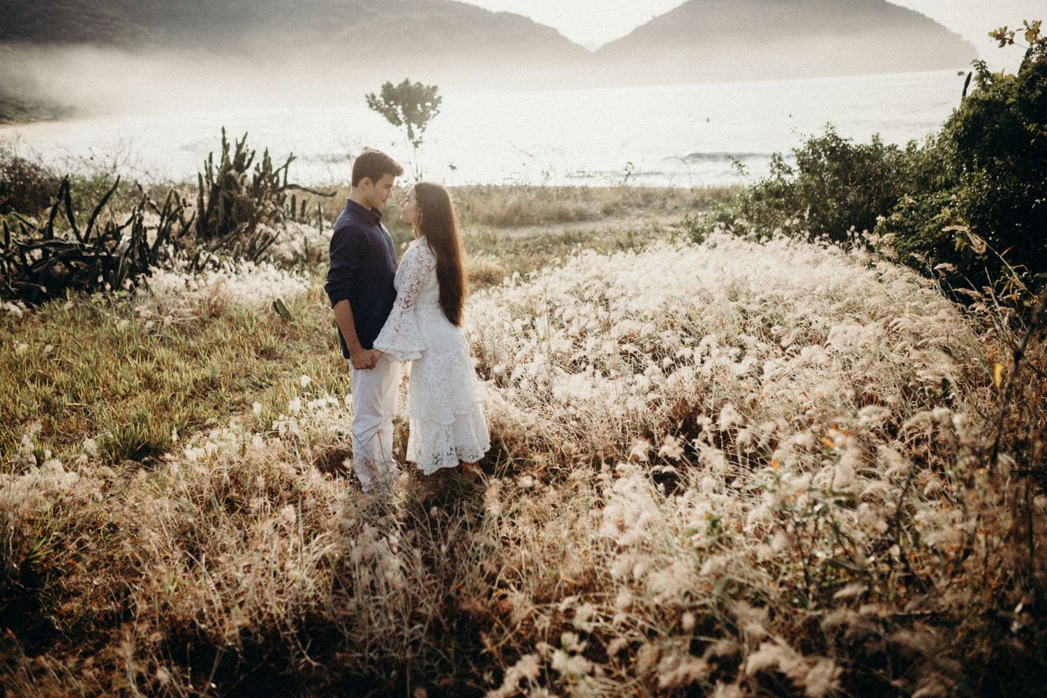 Romantic golden hour photoshoot in a hillside meadow with soft natural lighting.