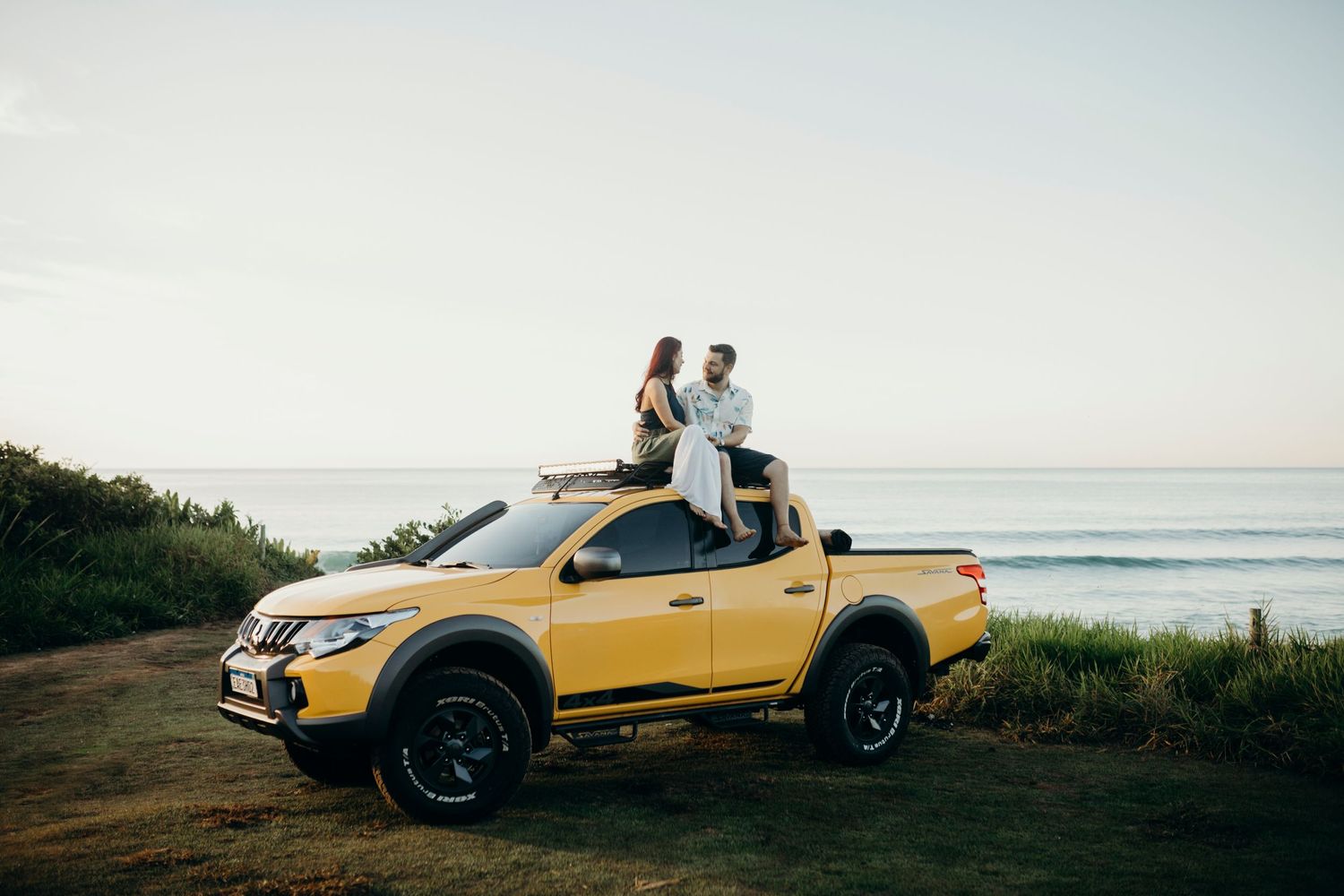 Yellow pickup truck parked on coastal overlook during golden hour.